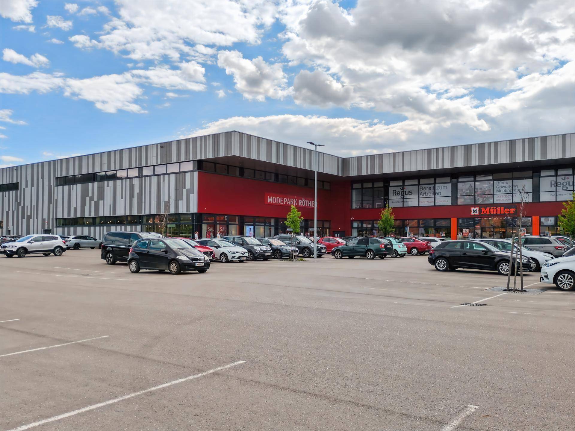 Großes modernes Geschäftsgebäude mit roter und gestreifter Fassade und einem weitläufigen Parkplatz davor.