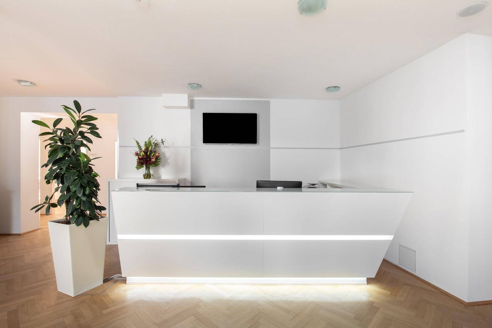 Moderner Empfangsbereich mit einer beleuchteten weißen Theke und einem Flachbildschirm an der Wand.