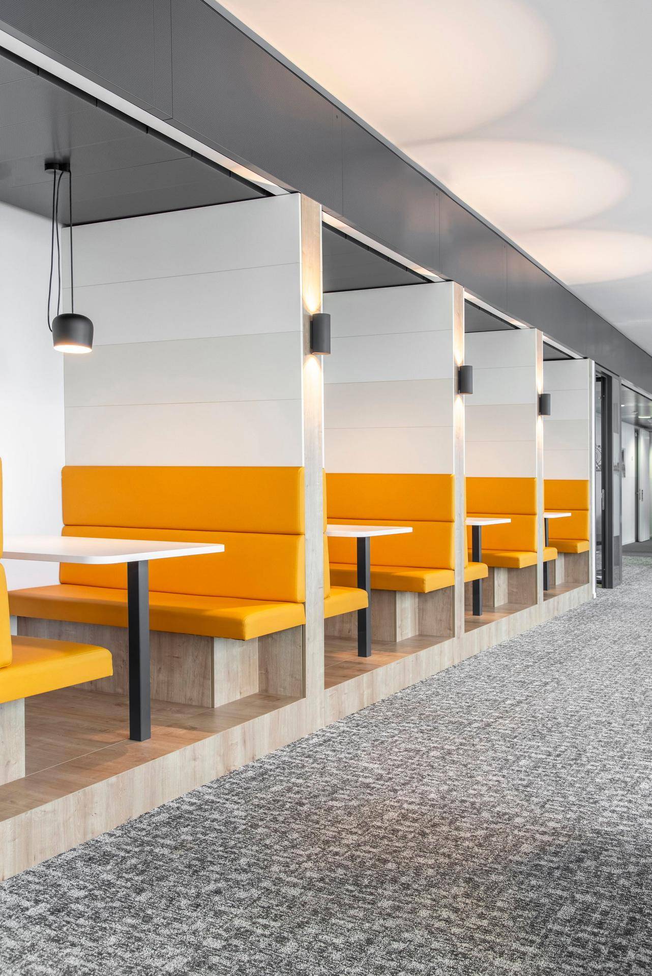 Reihe von modernen orangefarbenen Sitznischen mit kleinen Tischen, ideal für informelle Treffen oder Pausen.