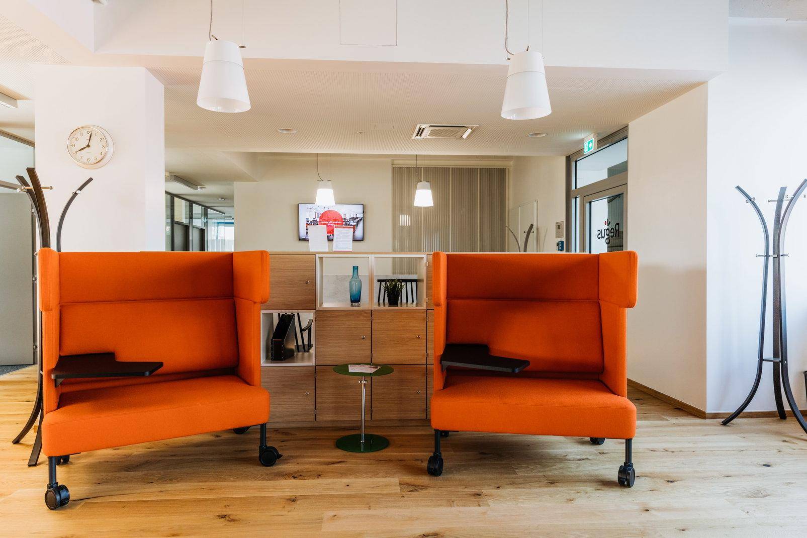 Gemütlicher Loungebereich mit orangefarbenen Sesseln, Holzregal und Pendelleuchten.
