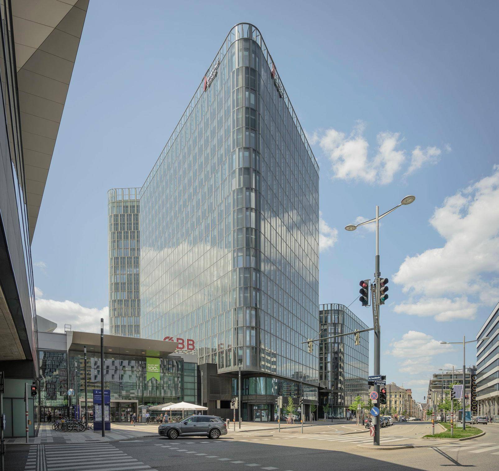 Modernes Bürogebäude mit Glasfassade an einer belebten Kreuzung unter blauem Himmel.