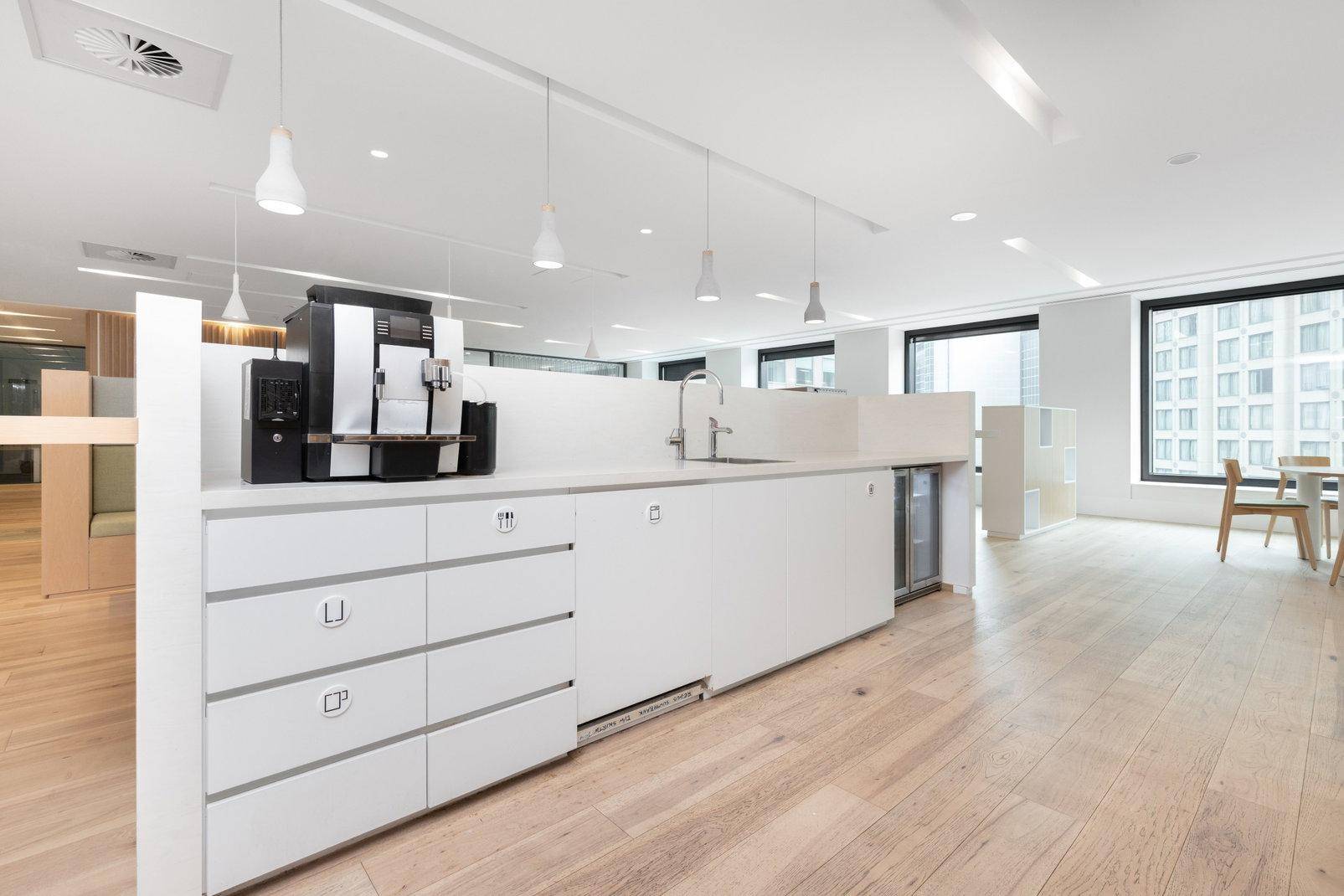 Helle Büroküche mit langer weißer Arbeitsplatte, Kaffeemaschine und Holzboden.