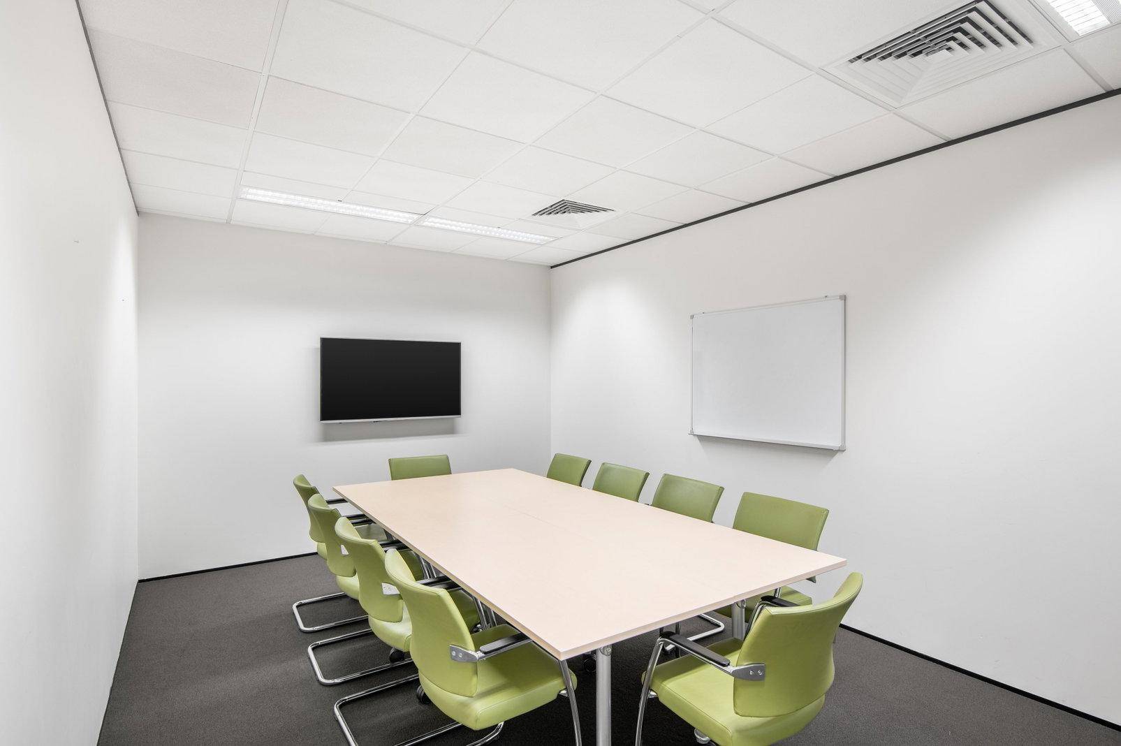 Konferenzraum mit großem Tisch, zehn grünen Stühlen, Wandfernseher und Whiteboard für Besprechungen.
