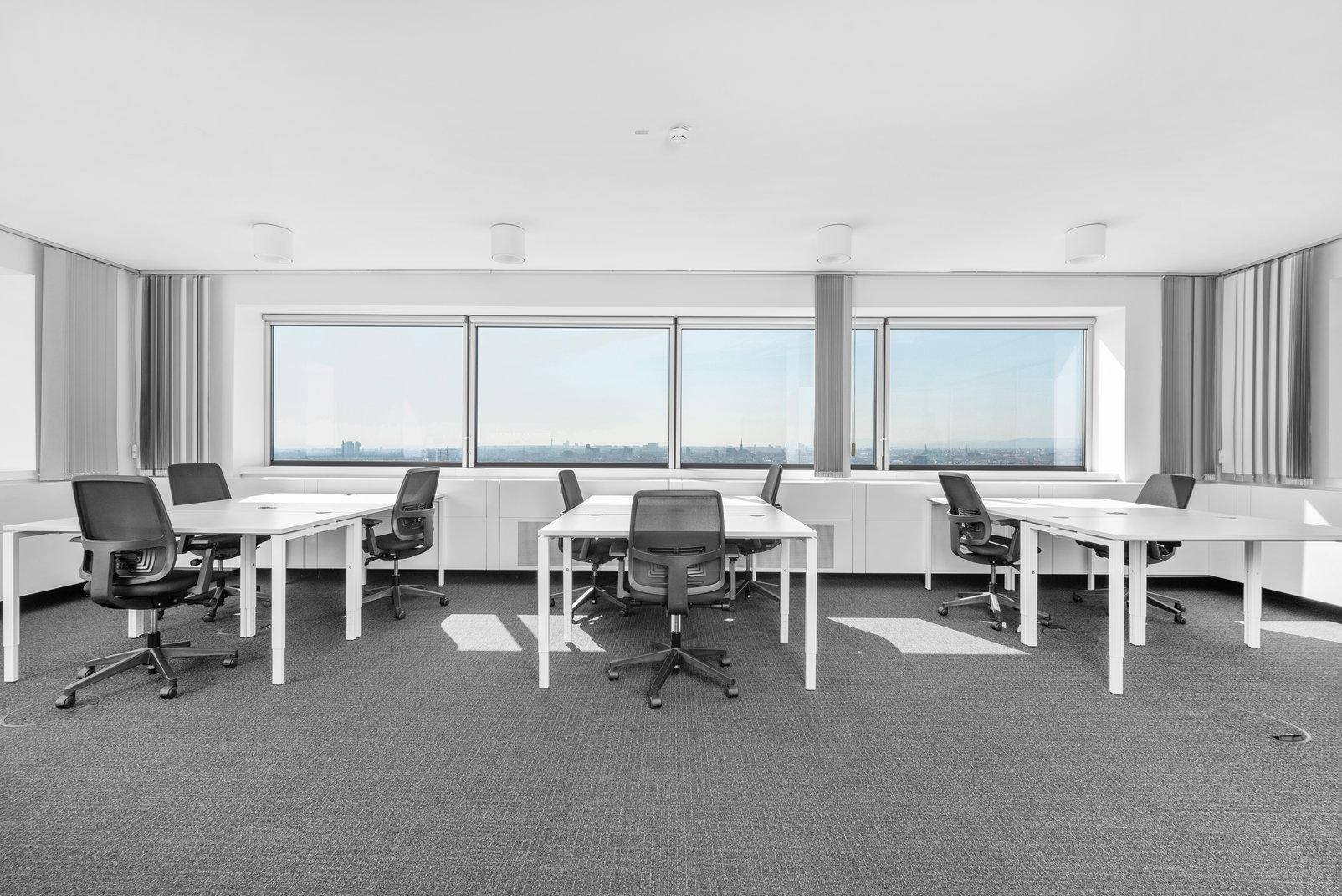Modernes Großraumbüro mit vielen Arbeitsplätzen, Teppichboden und weitem Ausblick durch große Fenster.