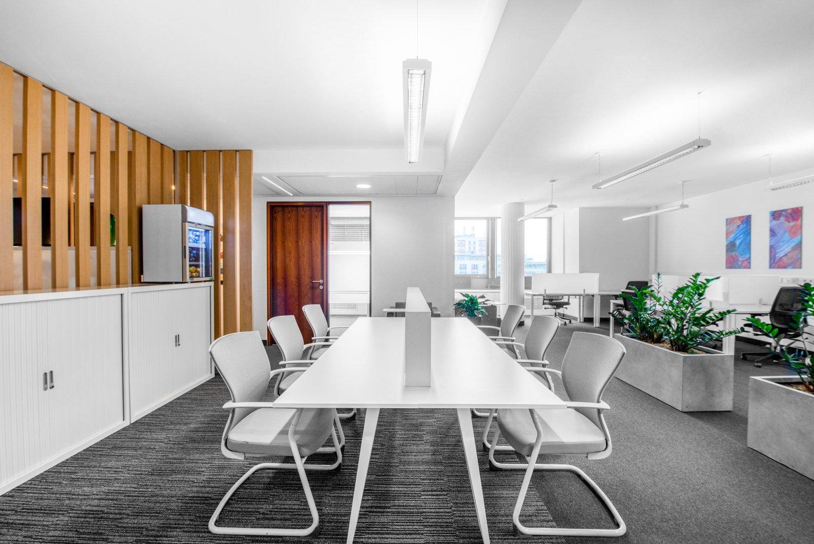 Helles Büro mit langem Konferenztisch, Holzlamellenwand, Pflanzen und modernen Büromöbeln.