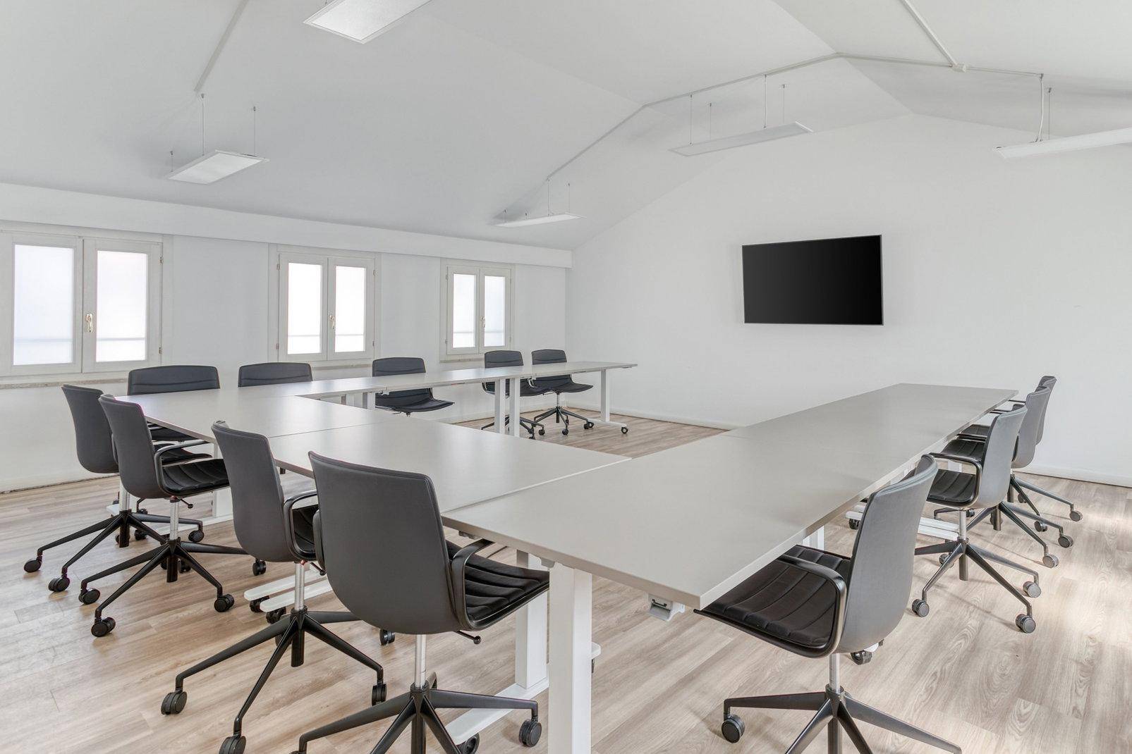 Heller Konferenzraum mit U-förmigem Tisch, modernen Stühlen und Holzboden unter Dachschrägen.