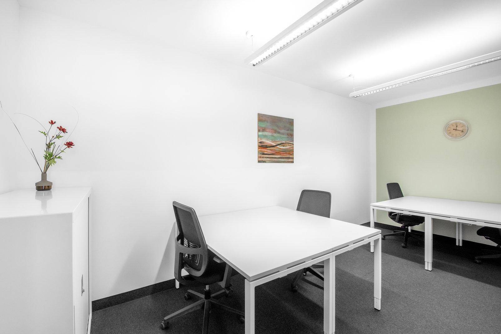 Kleines, helles Büro mit zwei Arbeitsplätzen, weißem Schrank und einer hellgrünen Akzentwand.