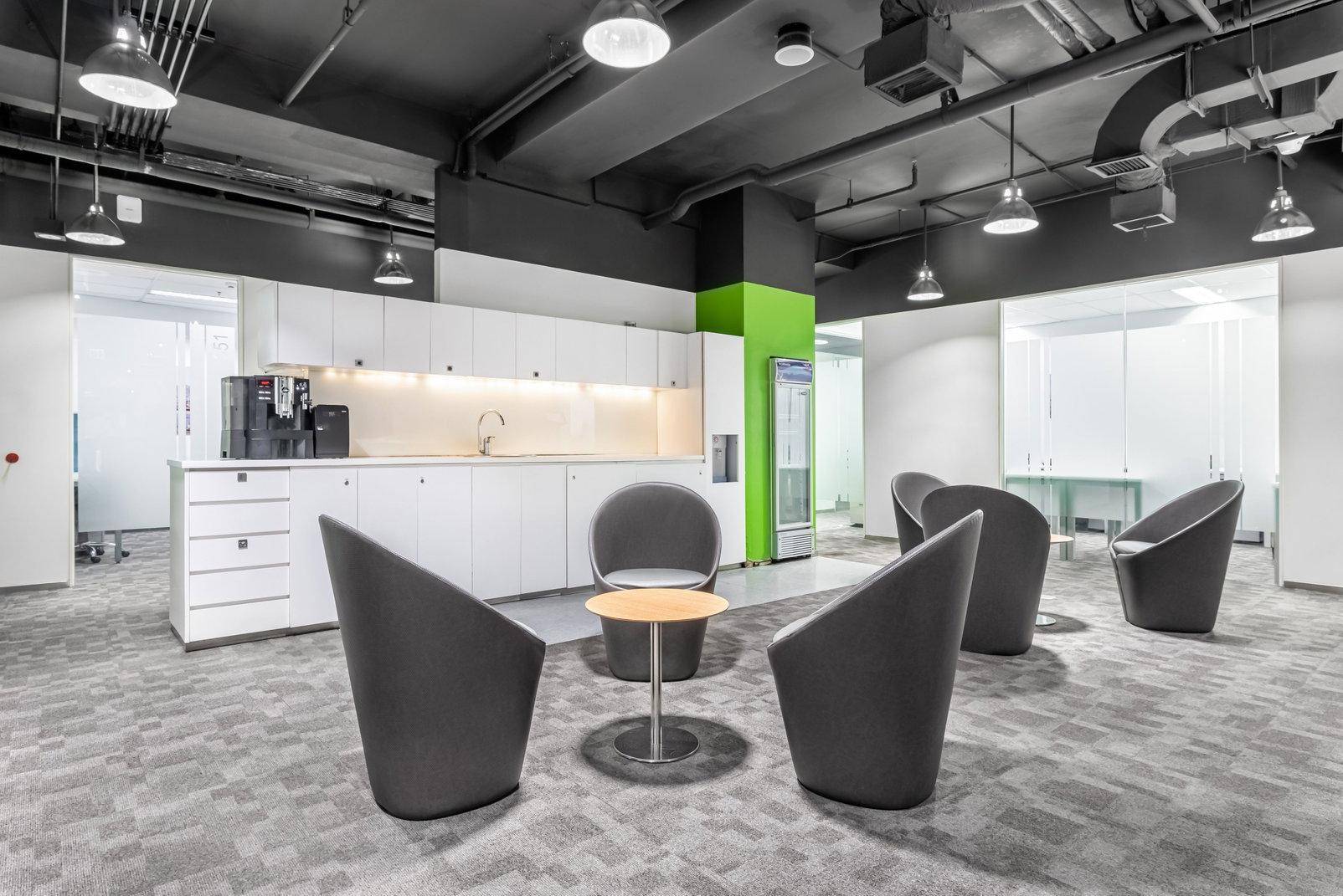 Moderne Büroküche mit weißen Schränken, schwarzer Decke und grauem Teppichboden in einem offenen Bereich.