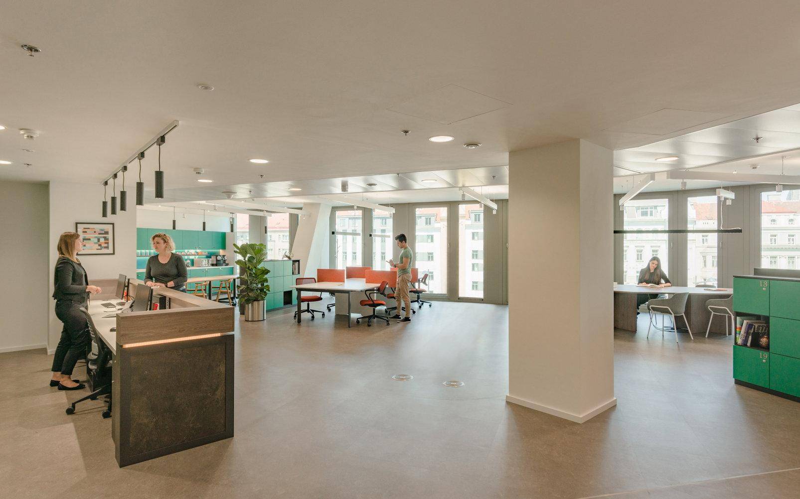 Offener Bürobereich mit Empfangstheke, verschiedenen Arbeitszonen und großen Fenstern für eine helle Atmosphäre.