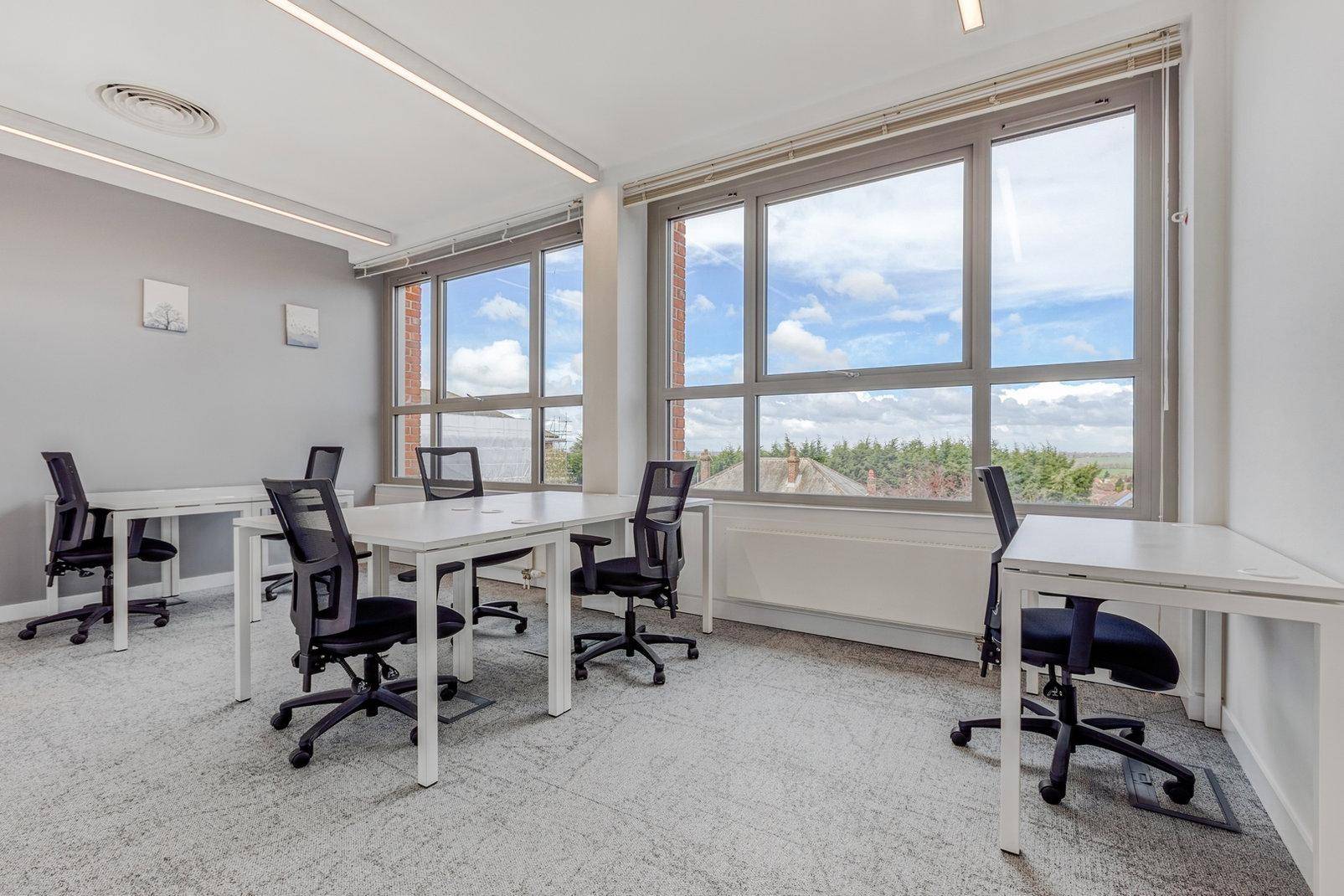 Helles Büro mit mehreren Arbeitsplätzen und großen Fenstern, die einen angenehmen Blick ins Grüne bieten.