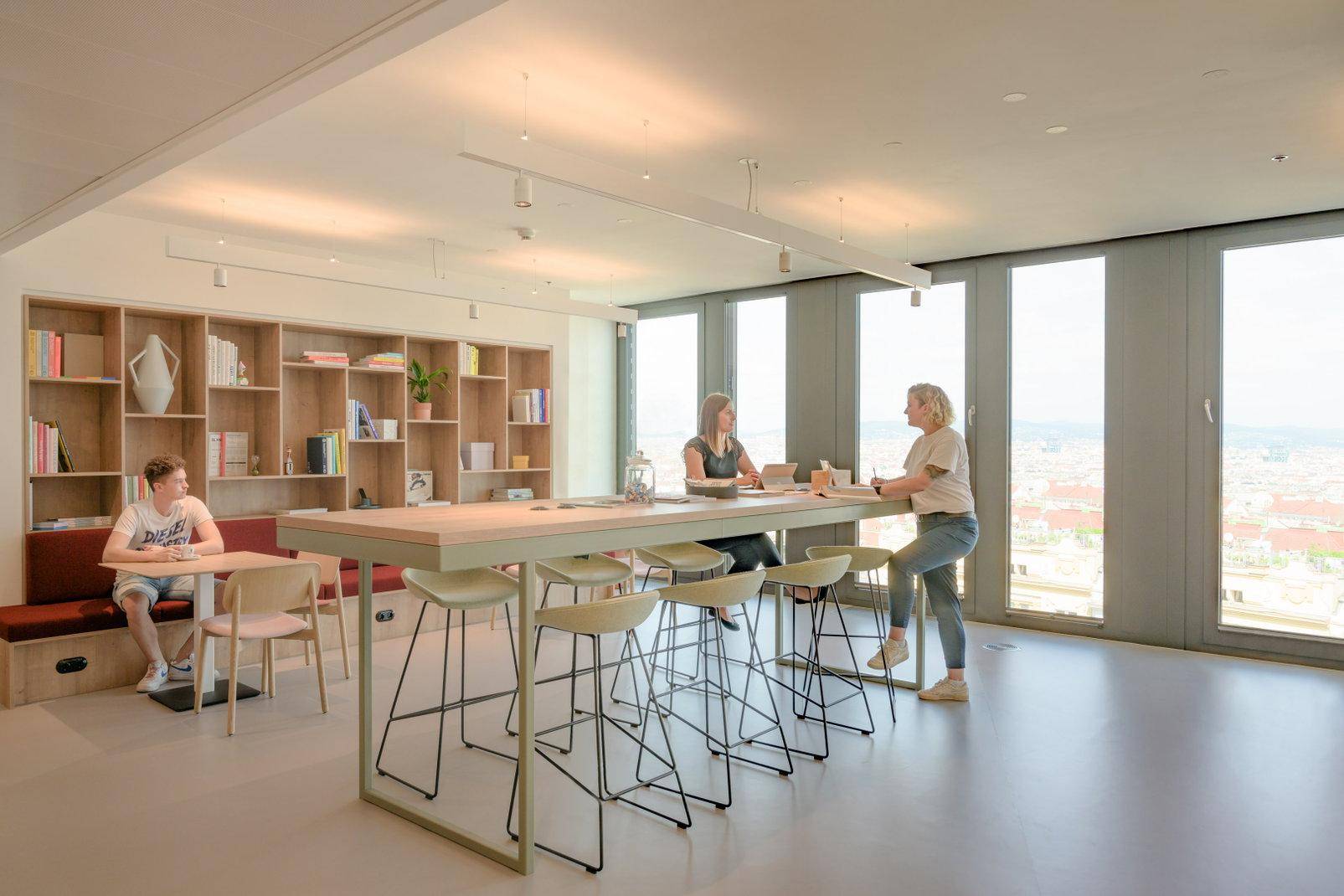 Moderner Loungebereich mit hoher Theke, Barhockern und einem großen Bücherregal an der Wand.