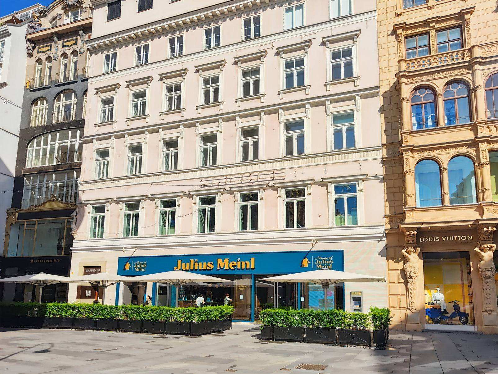 Historisches Gebäude mit klassischer Fassade und Geschäften im Erdgeschoss in einer belebten Straße.