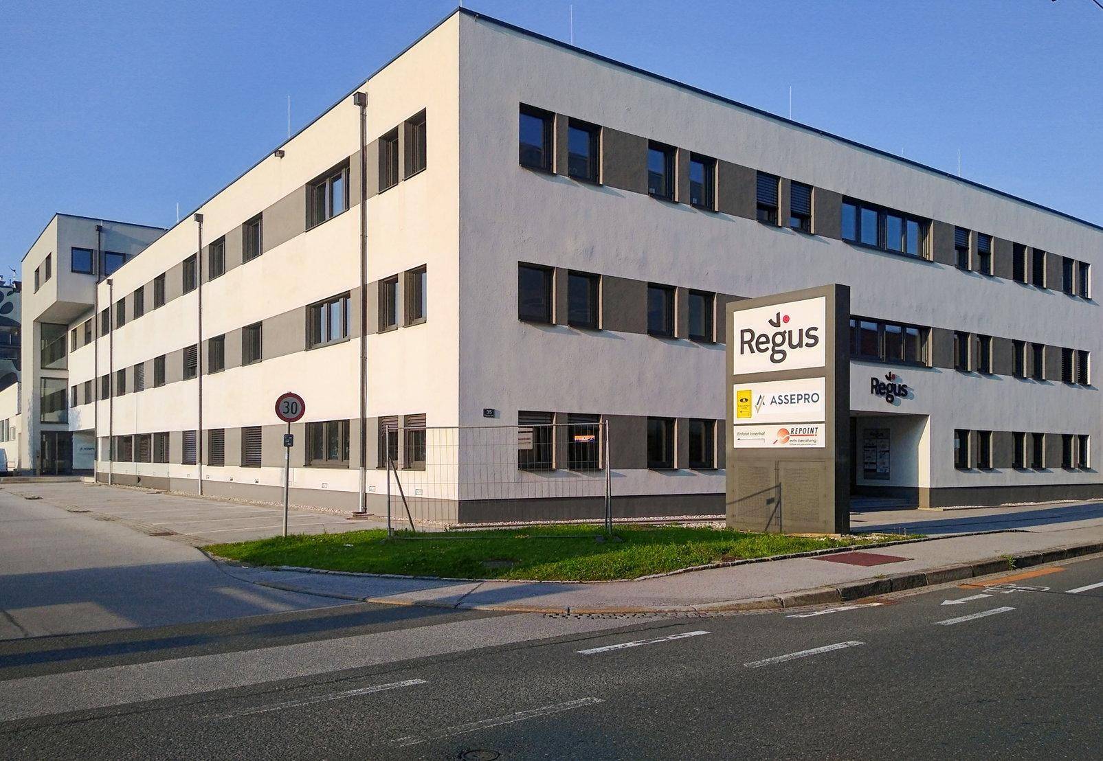 Modernes Bürogebäude mit weißer Fassade, vielen Fenstern und einem Regus-Schild an der Straßenseite.