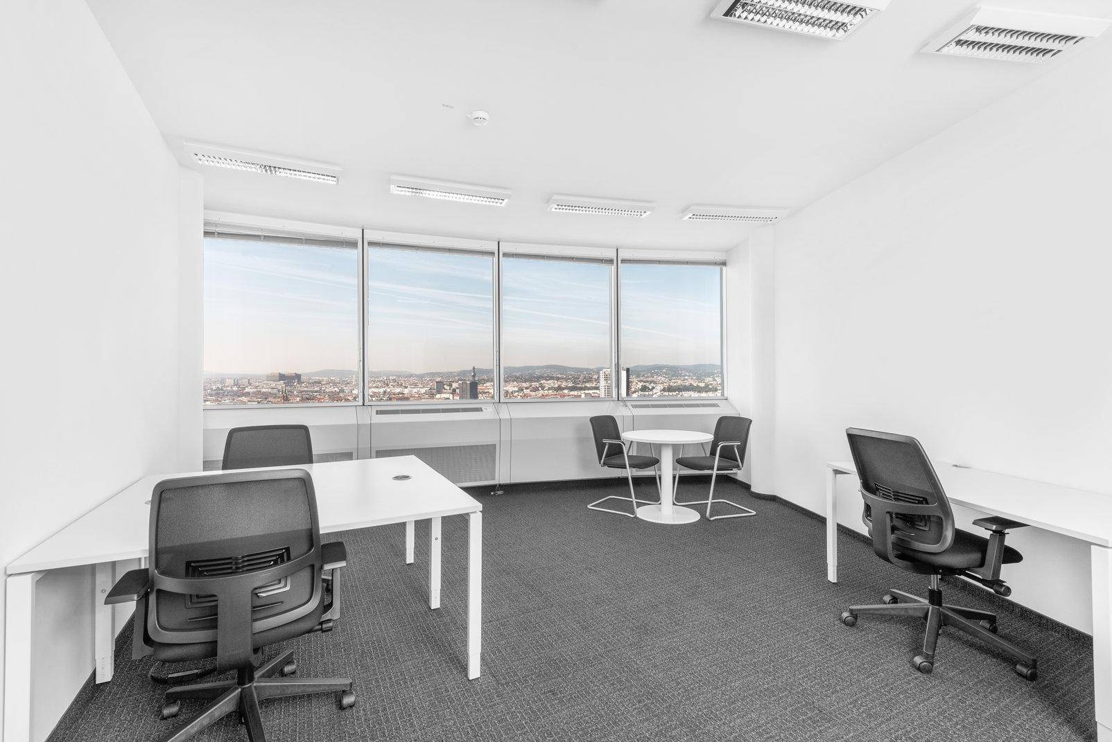 Helles Büro mit mehreren Arbeitsplätzen, Teppichboden und Panoramablick durch große Fenster.