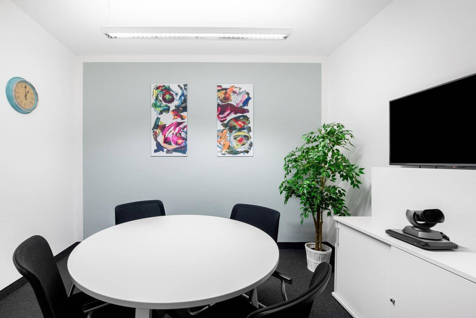 Kleiner Besprechungsraum mit rundem Tisch, Flachbildschirm und farbenfroher Kunst an der Wand.