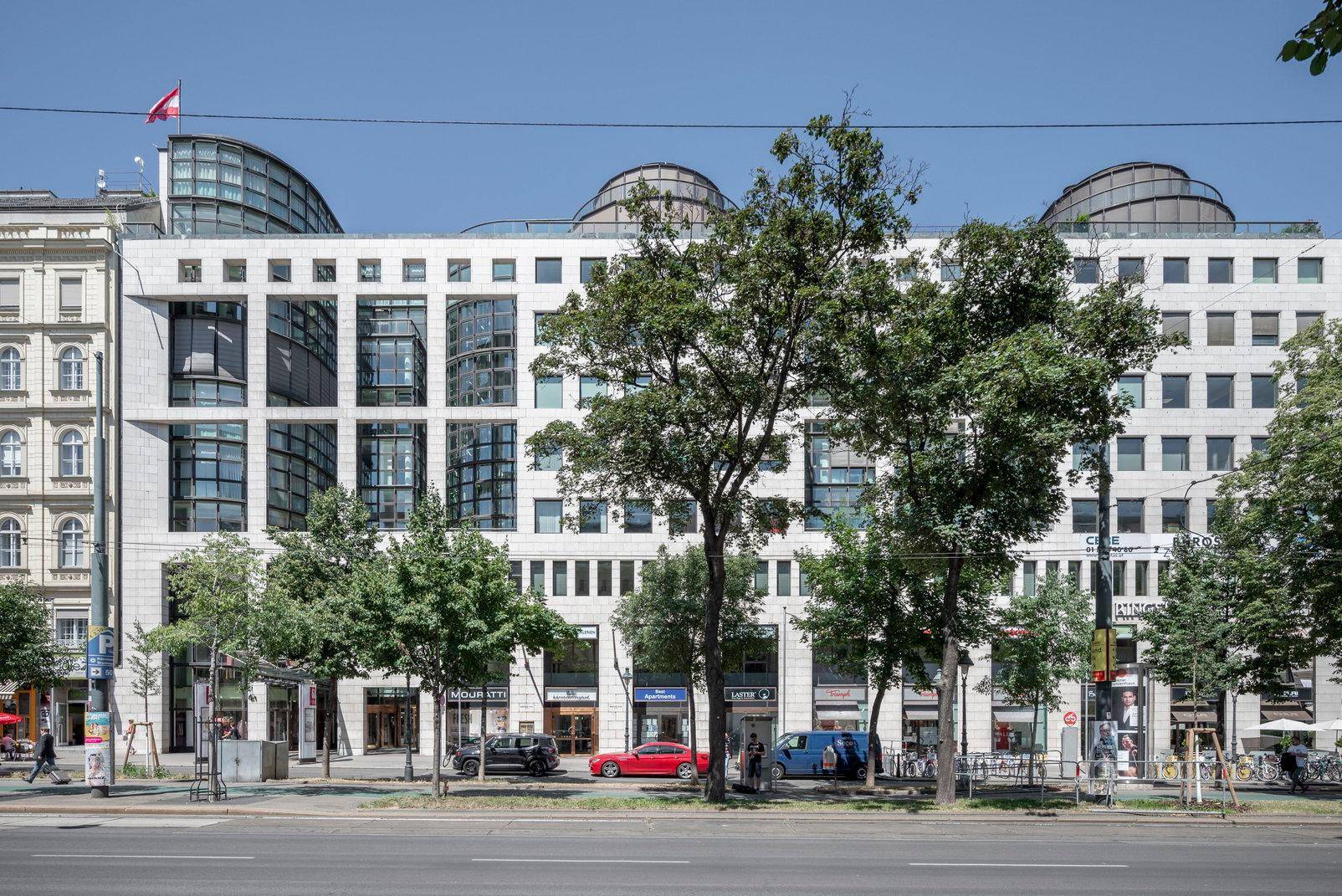 Moderne Bürogebäude-Fassade mit vielen Fenstern, Bäumen davor und einer belebten Straße.
