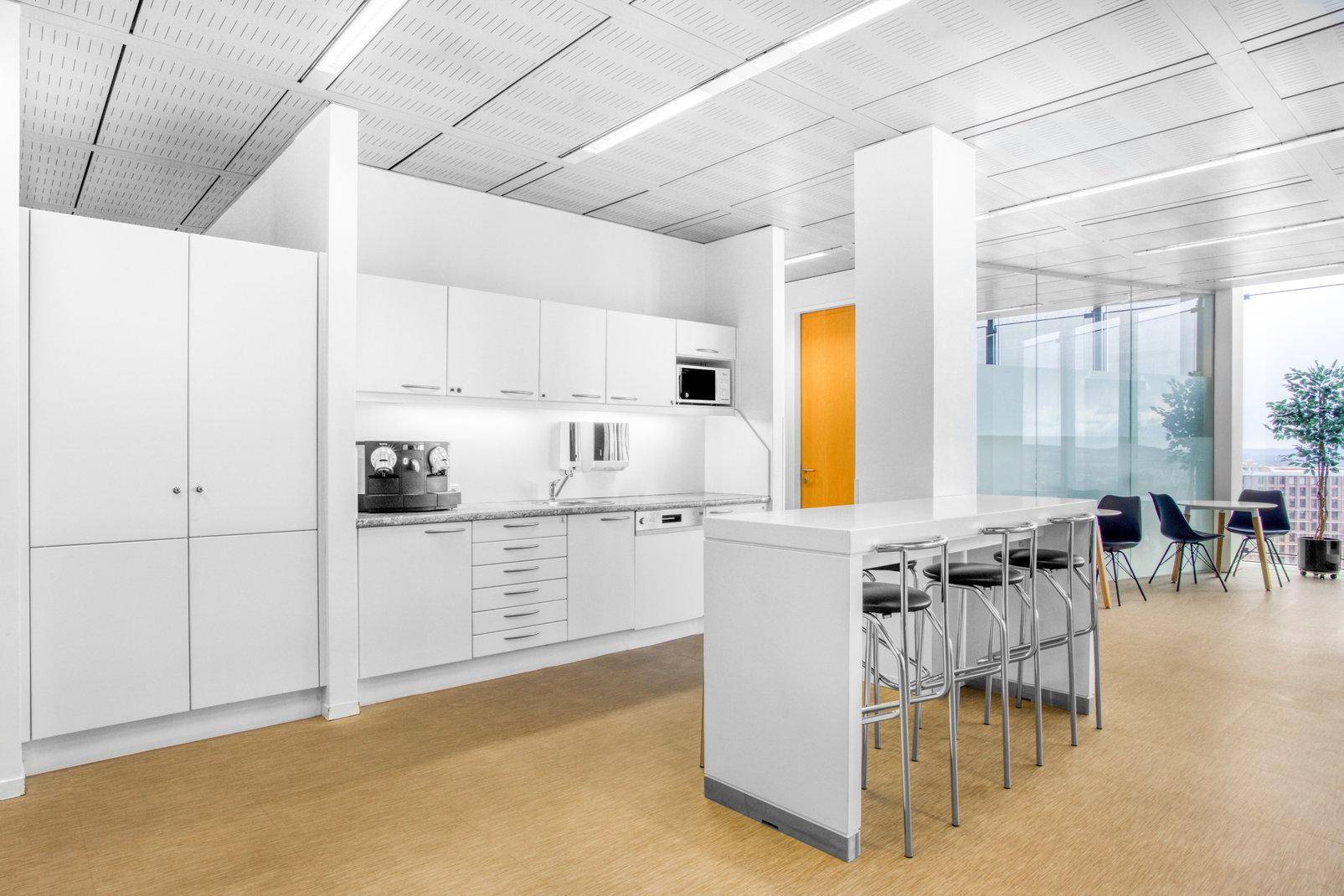 Moderne Büroküche mit weißen Schränken, Bartheke und integrierten Geräten.