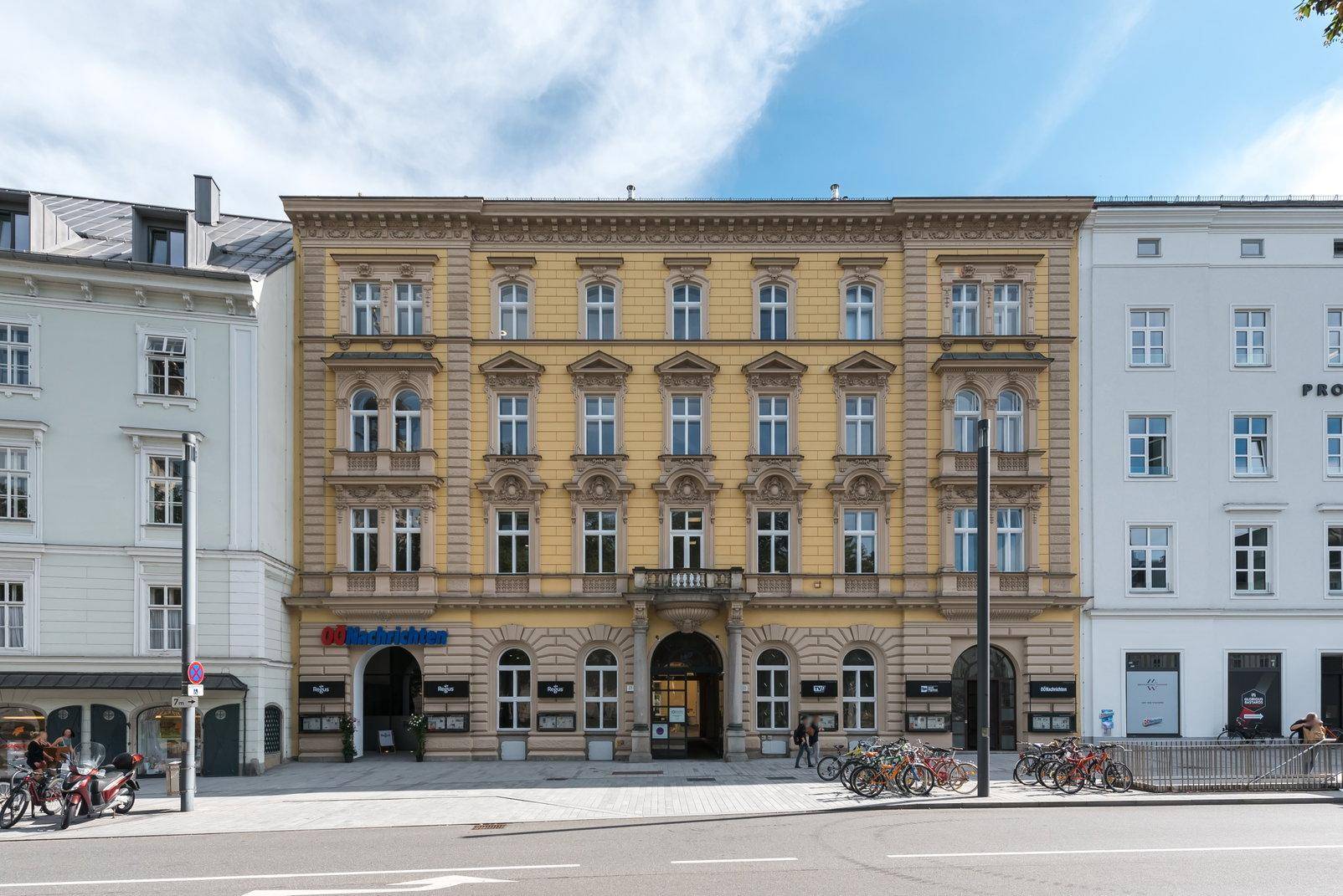 Historisches Gebäude mit gelber Fassade und vielen Fenstern an einer belebten Straße.