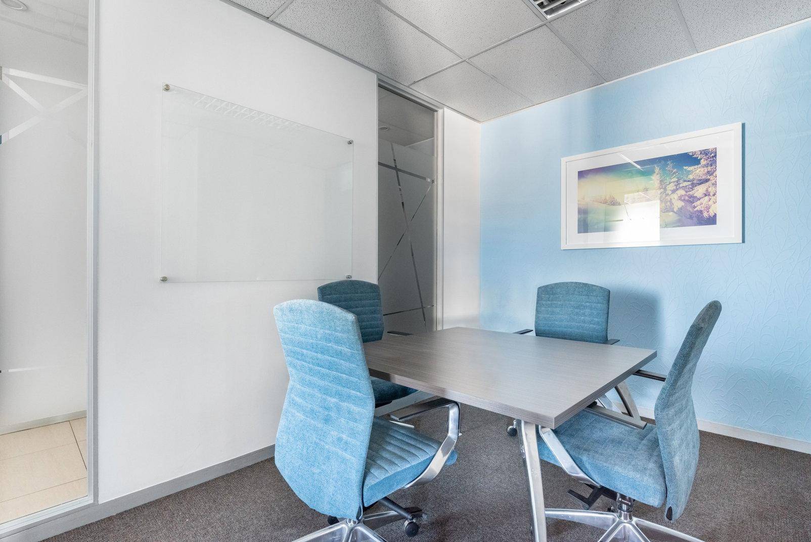 Kleiner Besprechungsraum mit blau gestrichener Wand, Glastür und vier Stühlen.