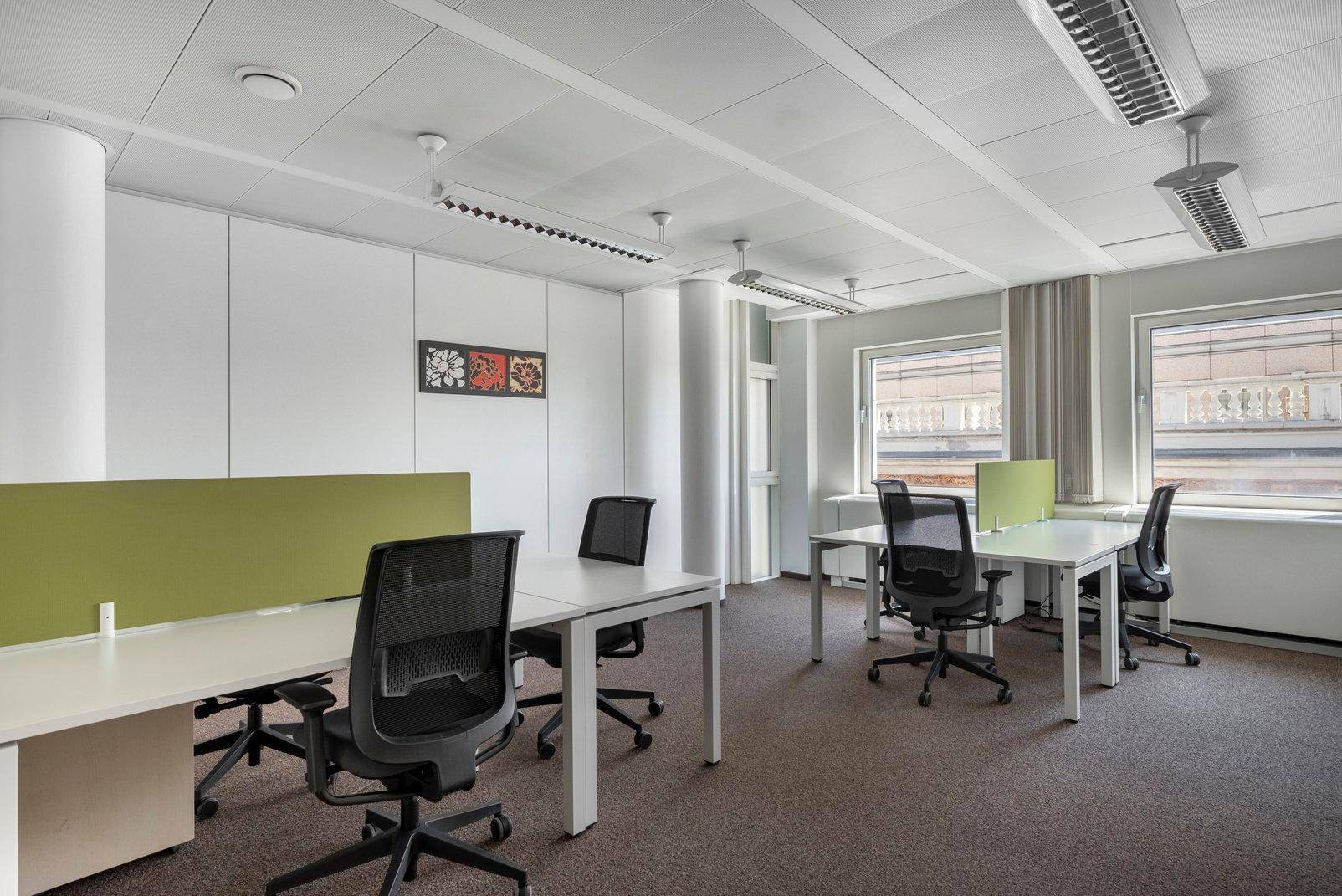 Offener Bürobereich mit mehreren Arbeitsplätzen, Teppichboden und Fenstern mit Blick nach draußen.