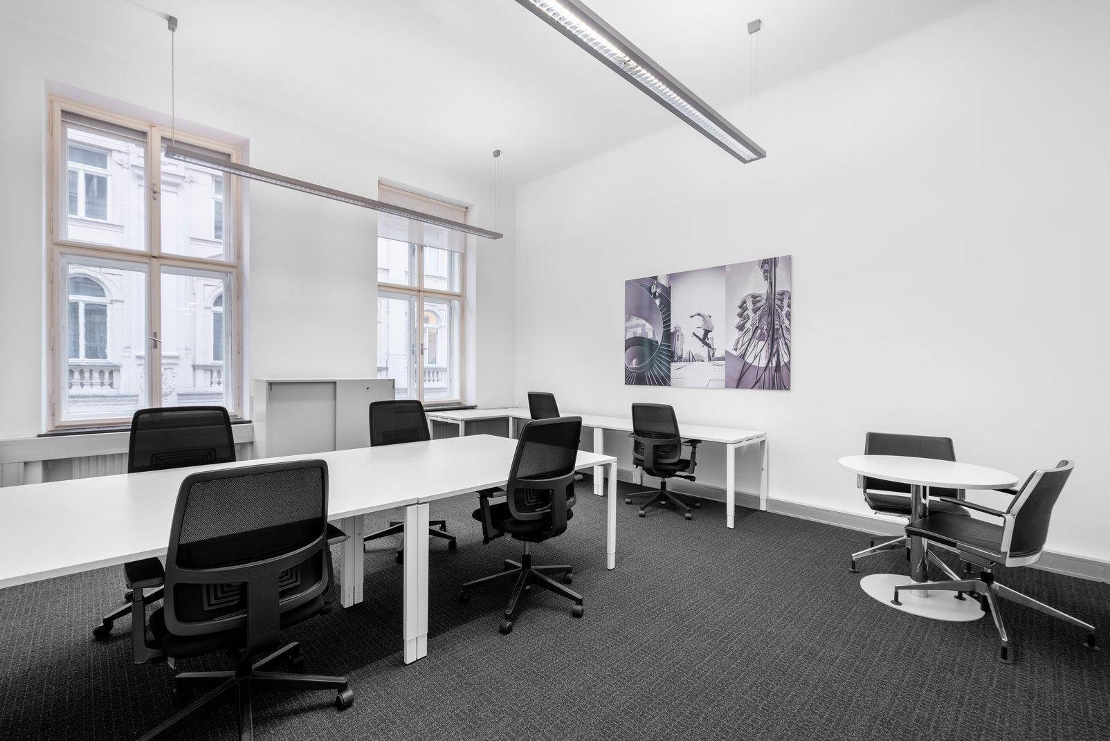 Geräumiges Büro mit mehreren Schreibtischen, ergonomischen Stühlen und großen Fenstern, die viel Licht hereinlassen.