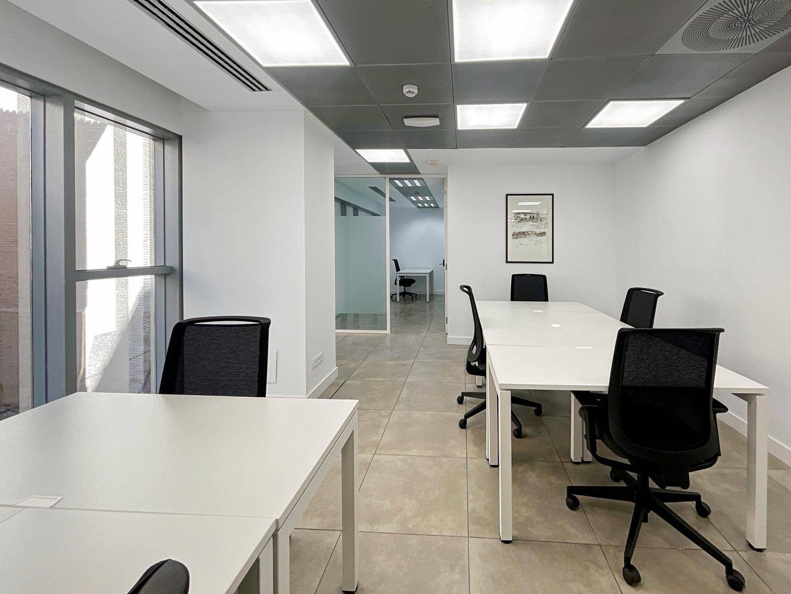 Modernes Büro mit mehreren Arbeitsplätzen, großen Fenstern und einem Blick in weitere Bürobereiche.