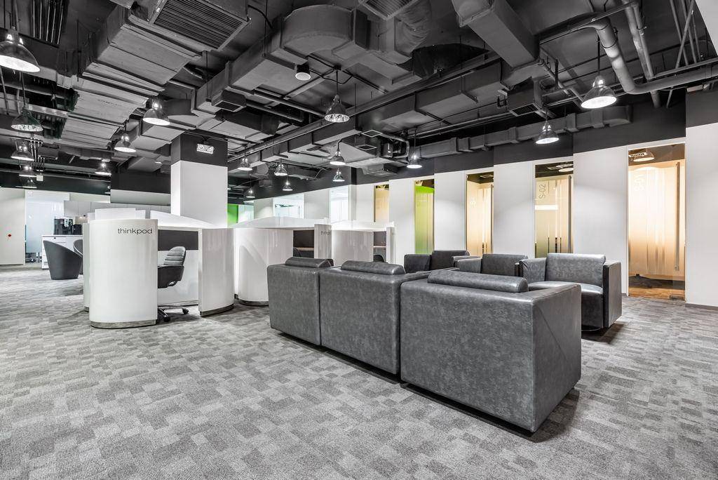 Großzügiger Bürobereich mit Lounge-Sitzgelegenheiten, Arbeitskabinen und industrieller Deckenästhetik.