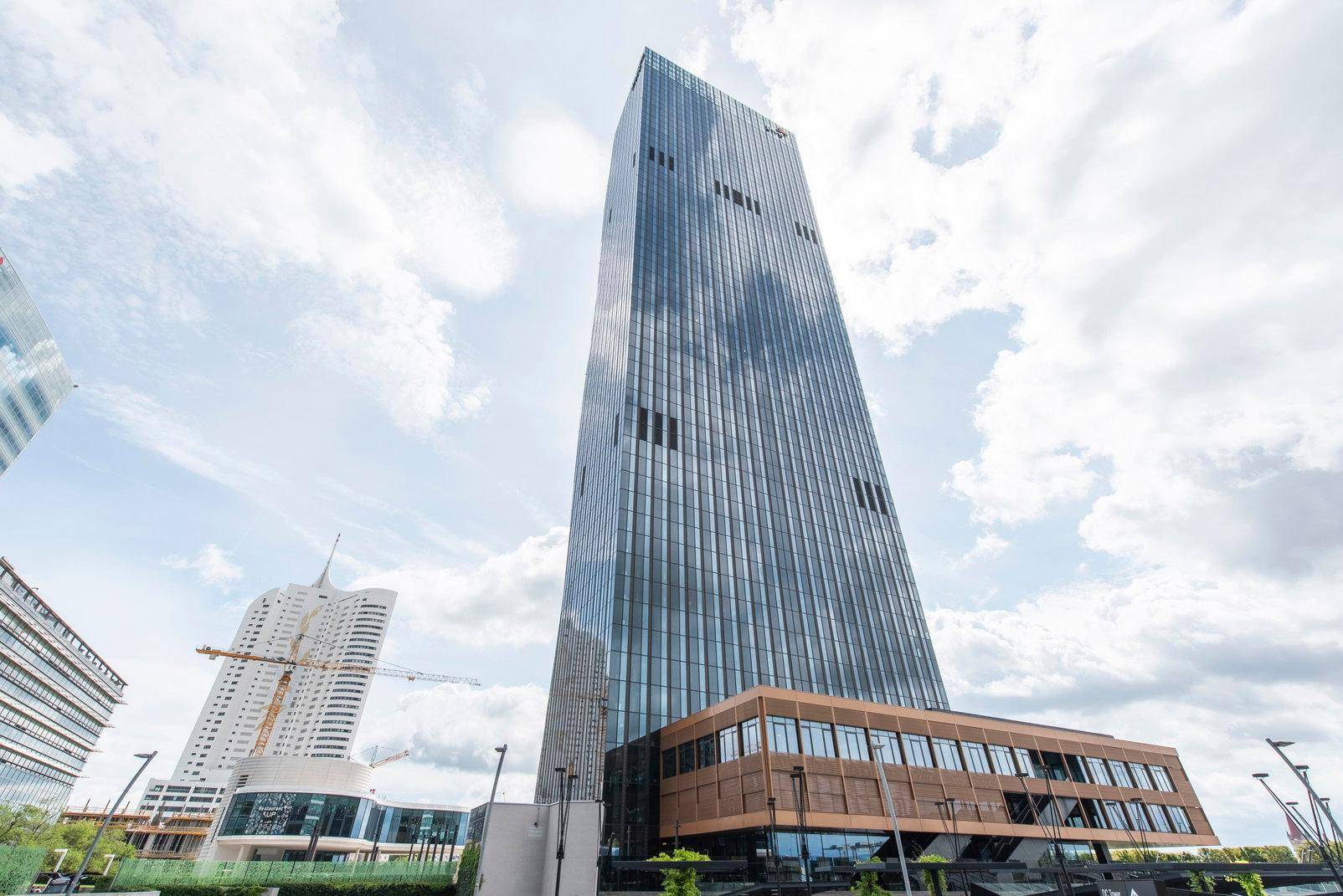 Beeindruckendes modernes Hochhaus mit Glasfassade unter einem weiten Himmel, umgeben von weiterer Bebauung.