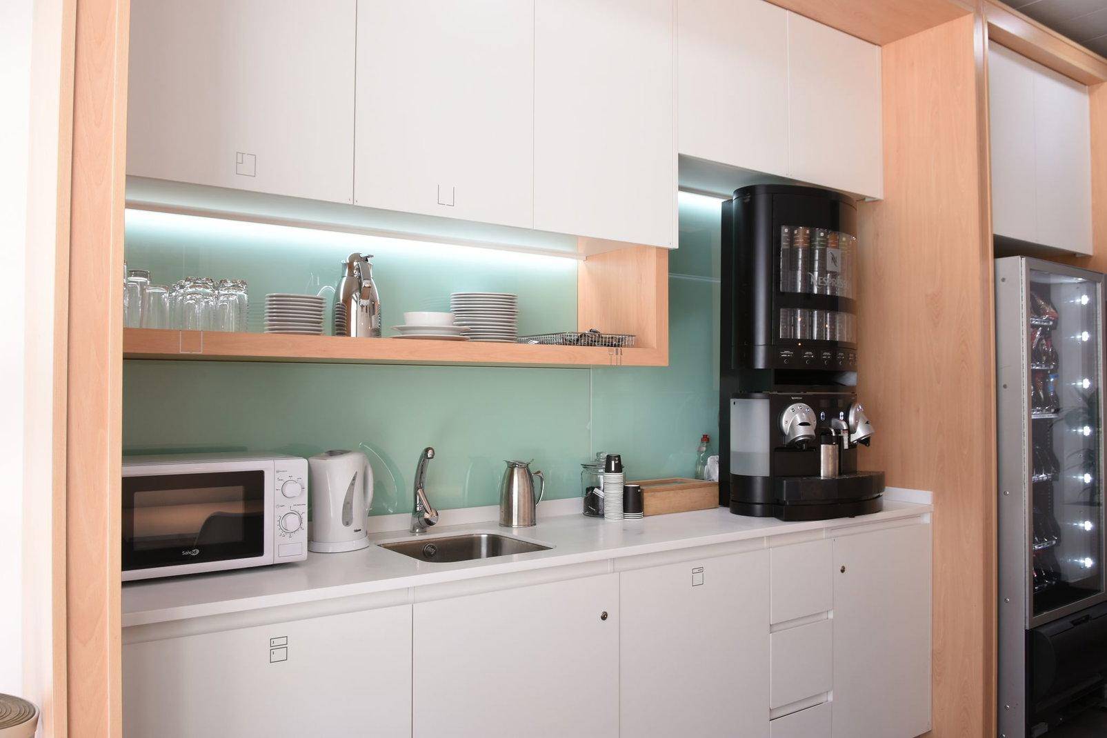 Moderne Teeküche mit weißen Schränken, Spüle, Mikrowelle und einer integrierten Kaffeemaschine.