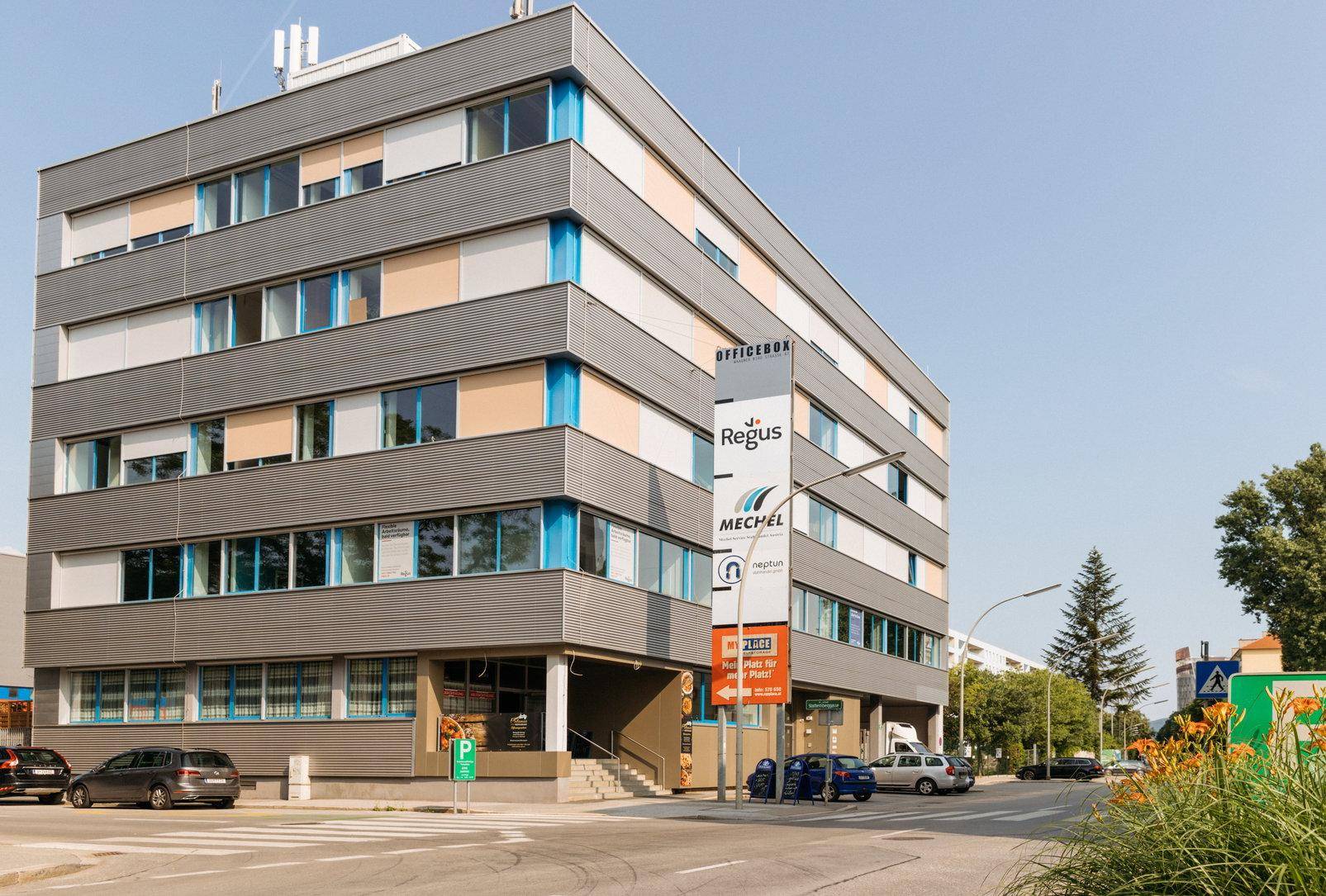 Modernes Bürogebäude mit mehreren Etagen, großen Fenstern und Werbeschildern an der Fassade.