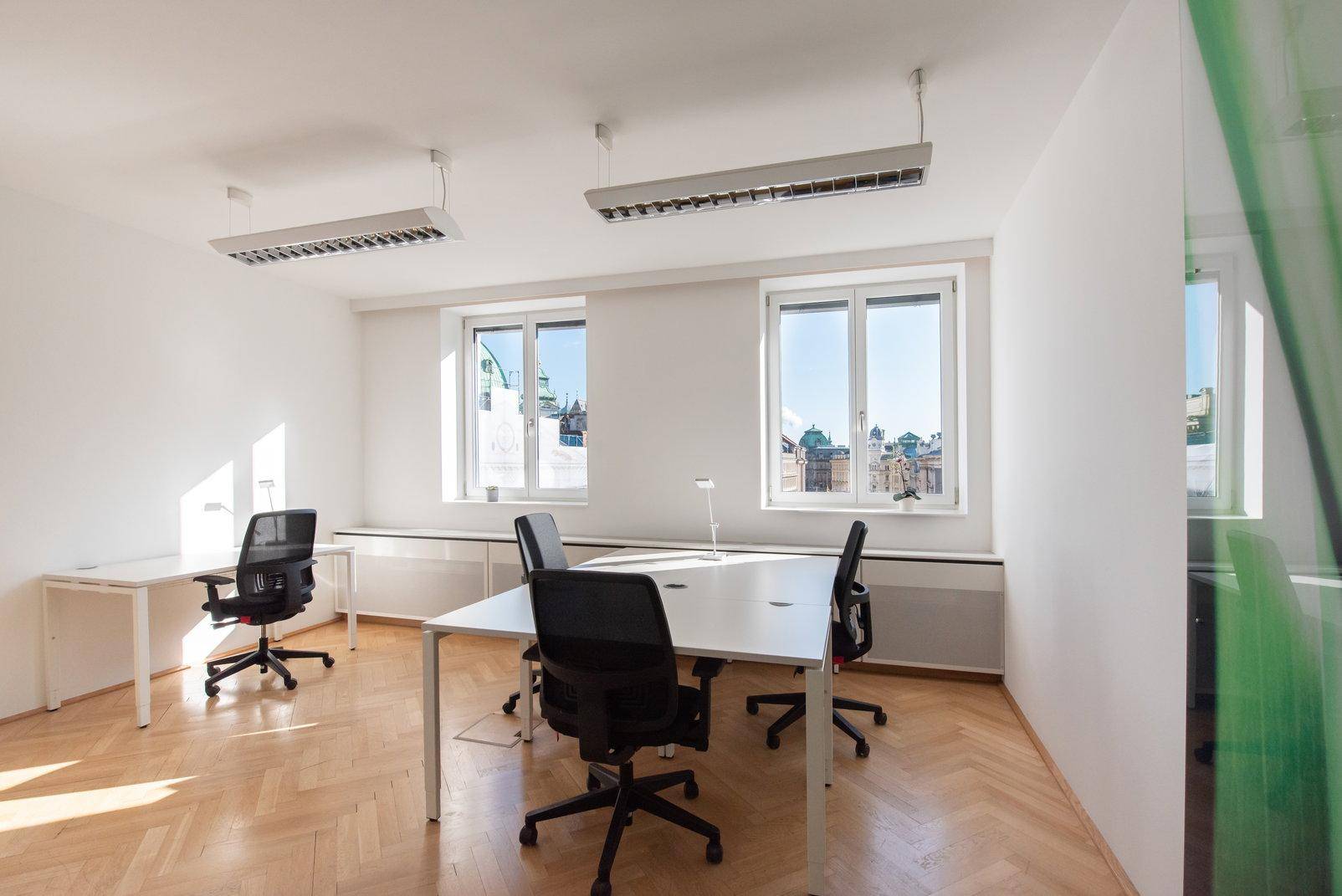 Geräumiges Büro mit mehreren Arbeitsplätzen, großen Fenstern und hellem Fischgrätparkettboden.