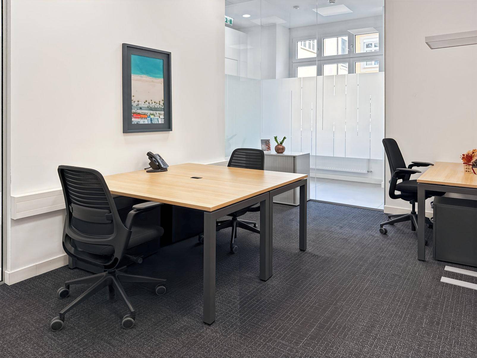 Helles Büro mit zwei Arbeitsplätzen, Teppichboden und Blick durch die Glastrennwand.