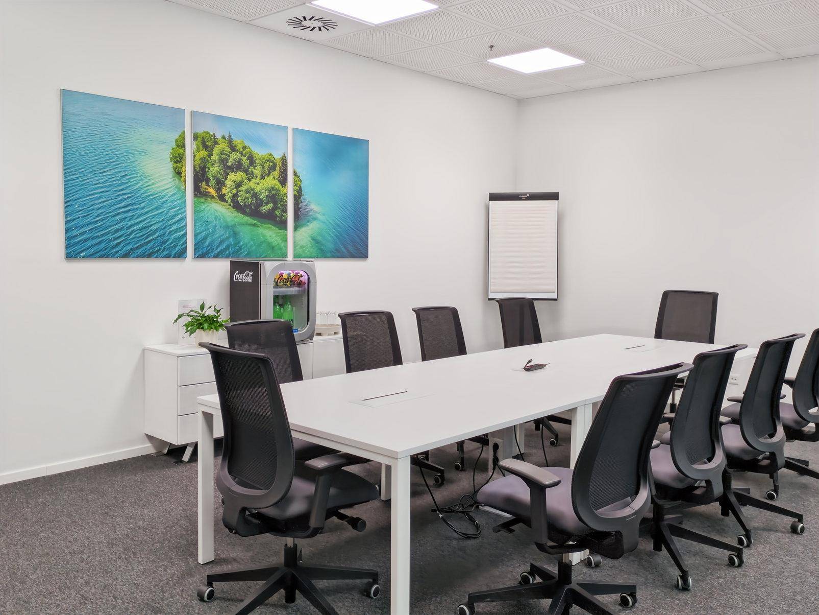 Konferenzraum mit langem Tisch, Bürostühlen, Flipchart und dekorativen Wandbildern mit Seeblick.