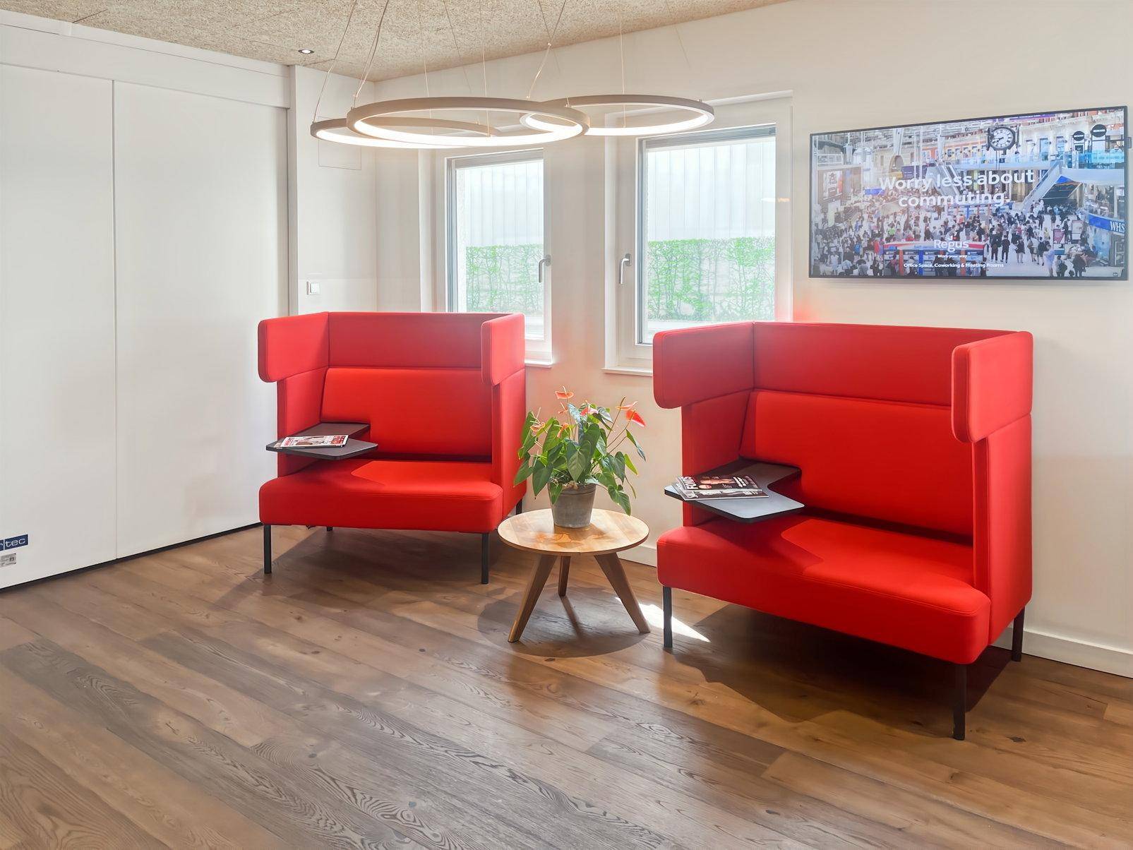 Moderner Loungebereich mit zwei roten Hochlehnsesseln, kleinem Beistelltisch und großen Fenstern für viel Licht.