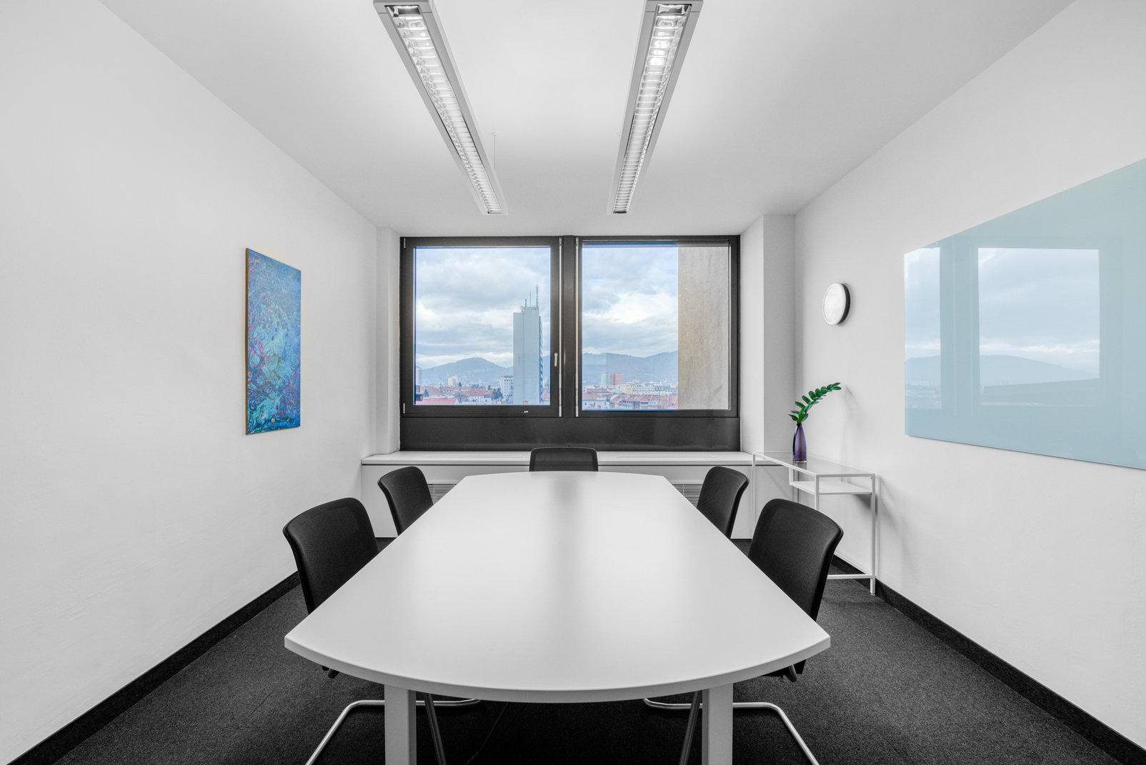 Konferenzraum mit großem Fenster, das einen weiten Blick auf die Stadt und Berge bietet.
