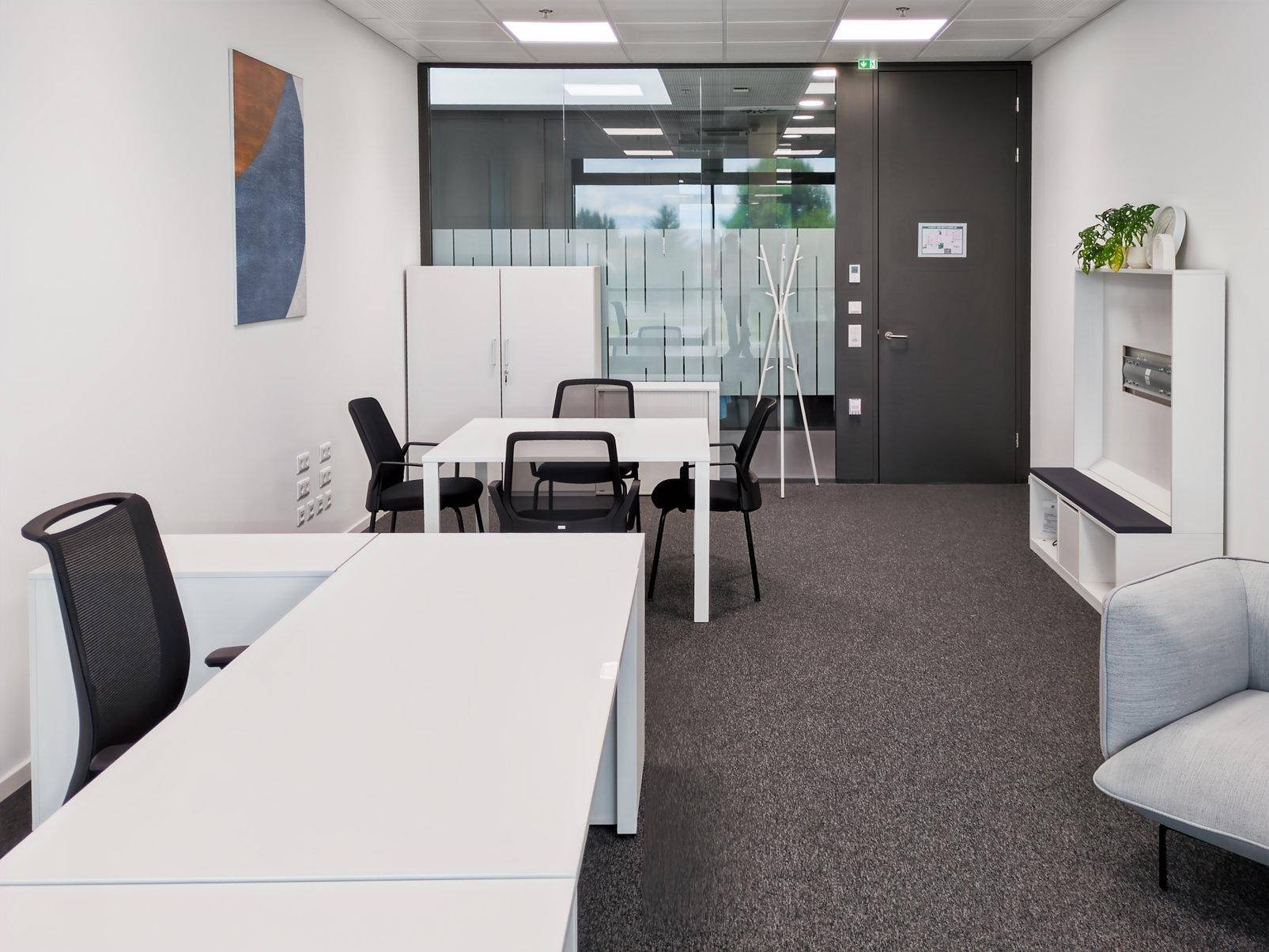 Helles Büro mit mehreren Arbeitsplätzen, Teppichboden und einer Garderobe am Eingangsbereich.