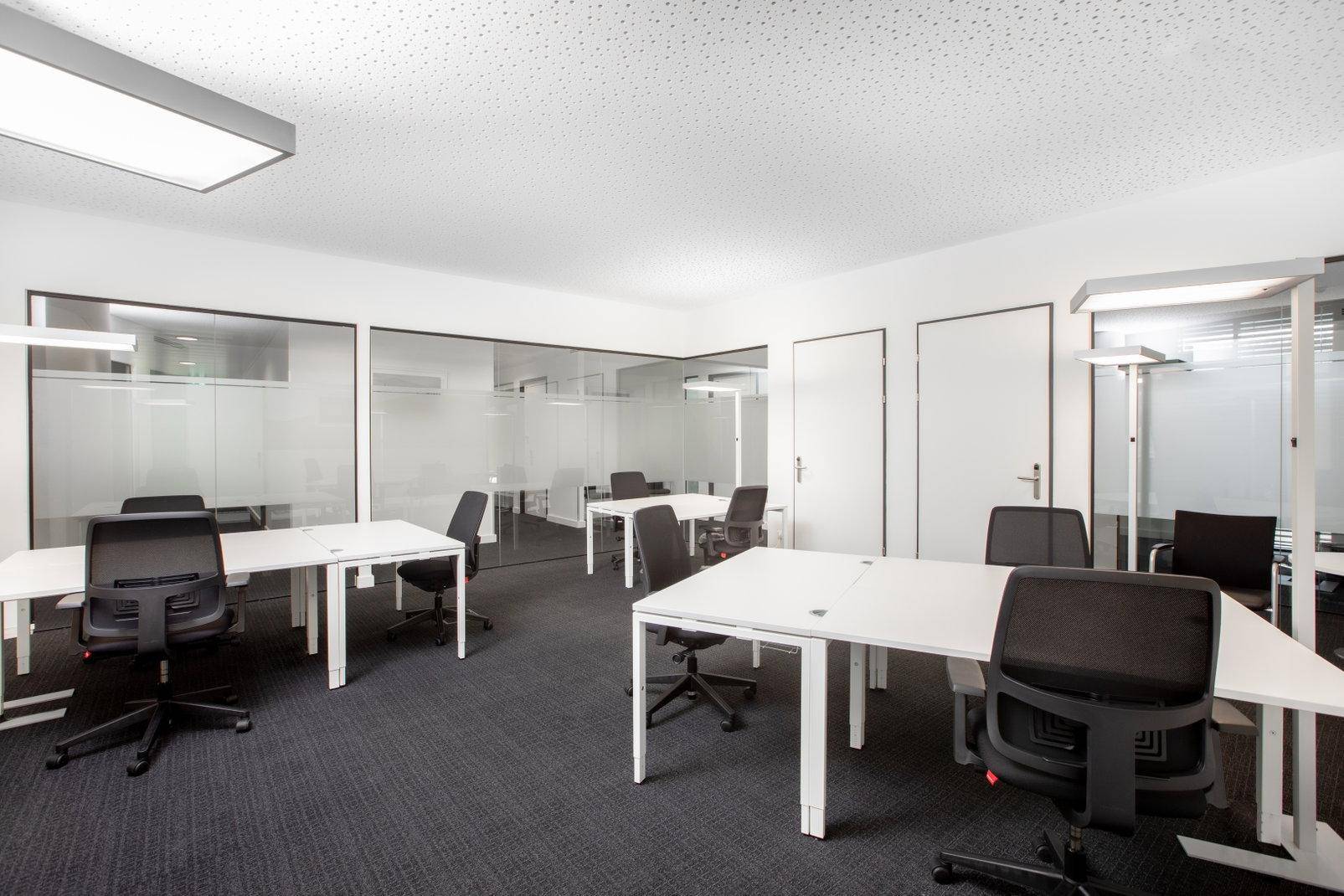 Modernes Großraumbüro mit mehreren Arbeitsplätzen, Teppichboden und Glaswänden für separate Bereiche.
