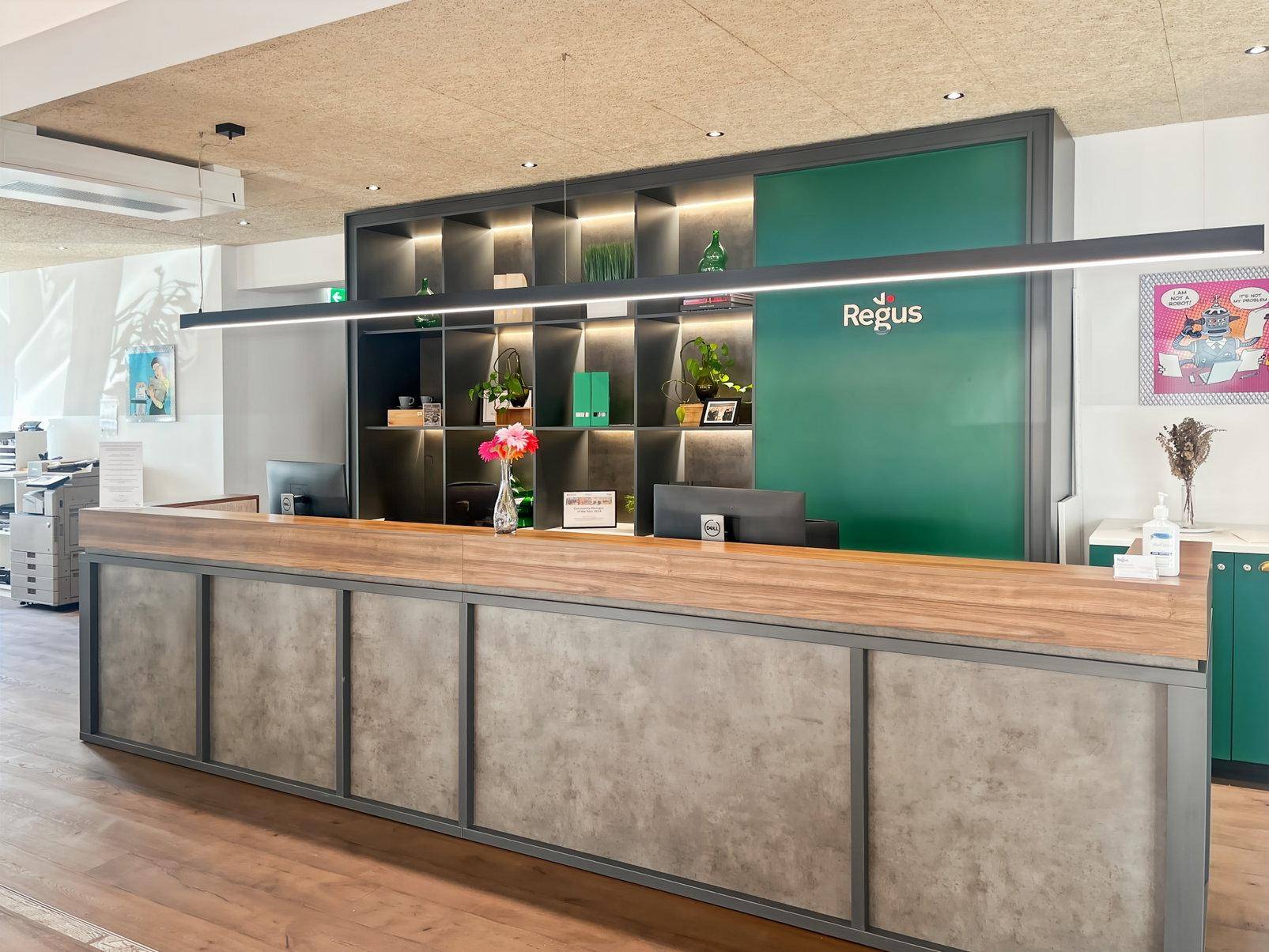 Empfangsbereich mit moderner Theke aus Holz und Betonoptik, grünen Regalen und Beleuchtung.