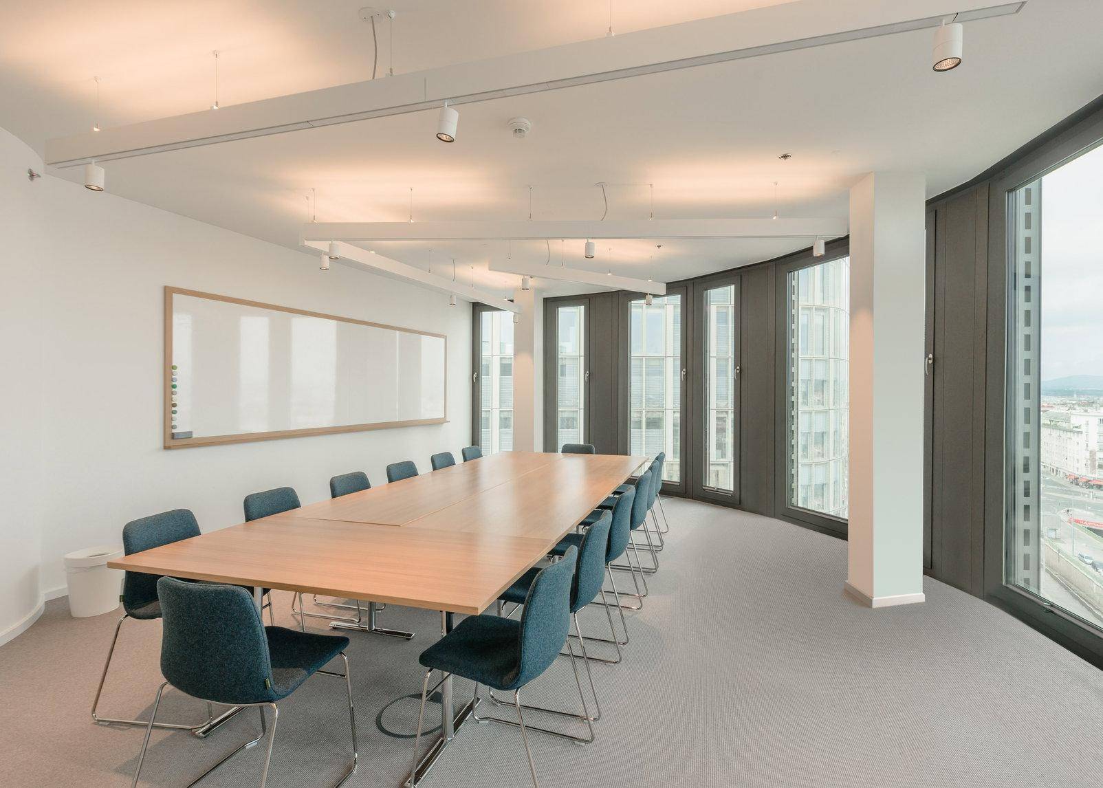 Moderner Konferenzraum mit großem Tisch, vielen Stühlen und Panoramafenstern mit Stadtblick.
