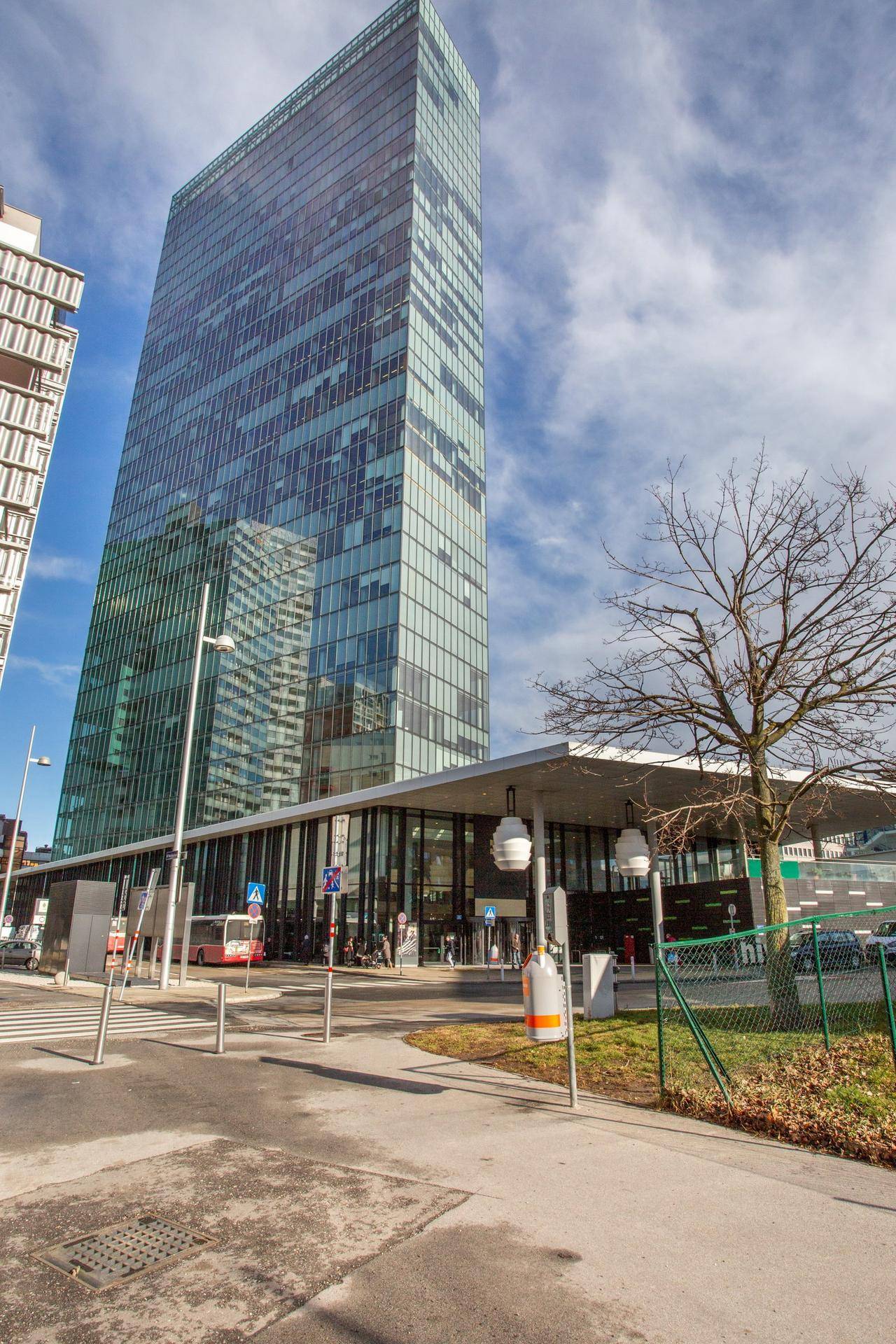 Hohes, modernes Bürogebäude mit Glasfassade und umliegender Infrastruktur unter blauem Himmel.