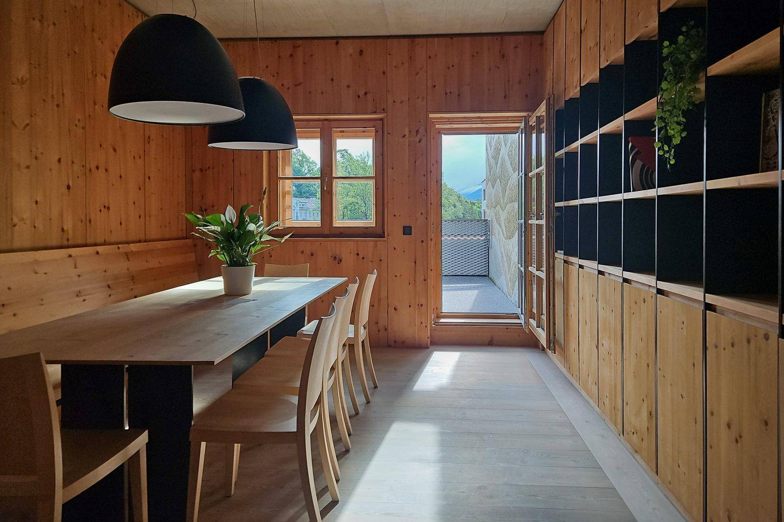 Rustikaler Essbereich mit Holztäfelung, langem Holztisch, modernen Pendelleuchten und Zugang zum Balkon.