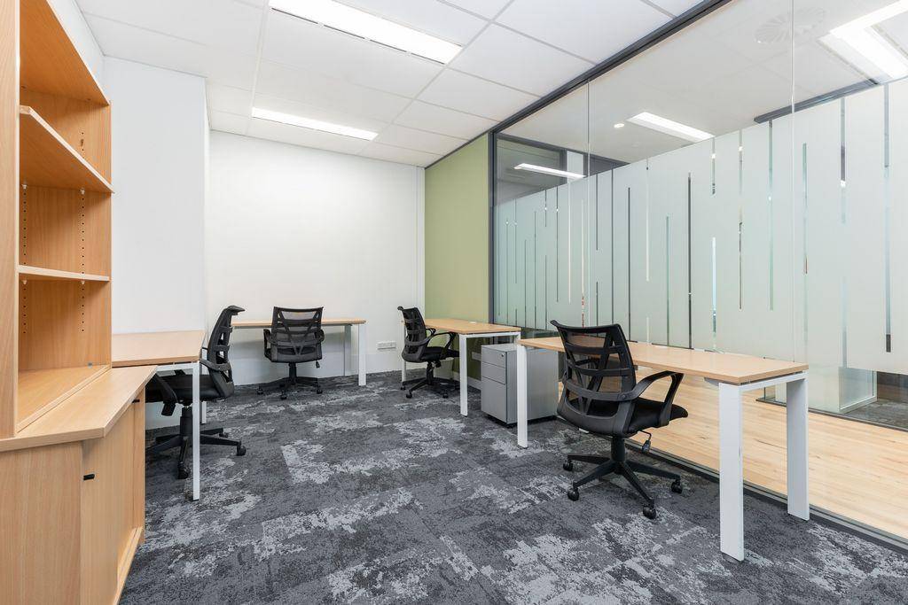 Geräumiges Büro mit Holzschreibtischen, ergonomischen Stühlen und einer modernen Glaswand als Raumteiler.