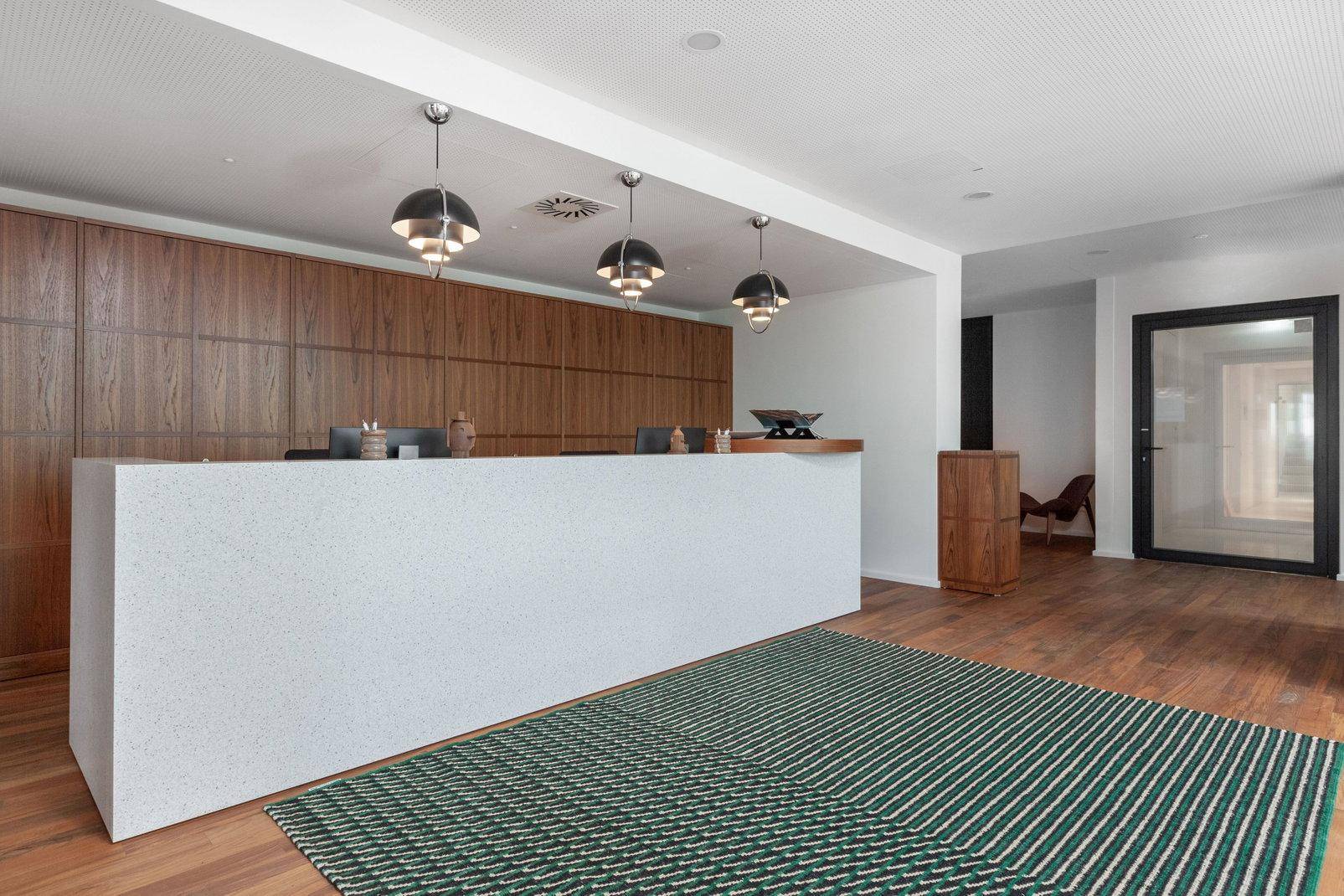 Elegante Empfangshalle mit einer langen weißen Theke, Holzvertäfelung und dekorativen Pendelleuchten.