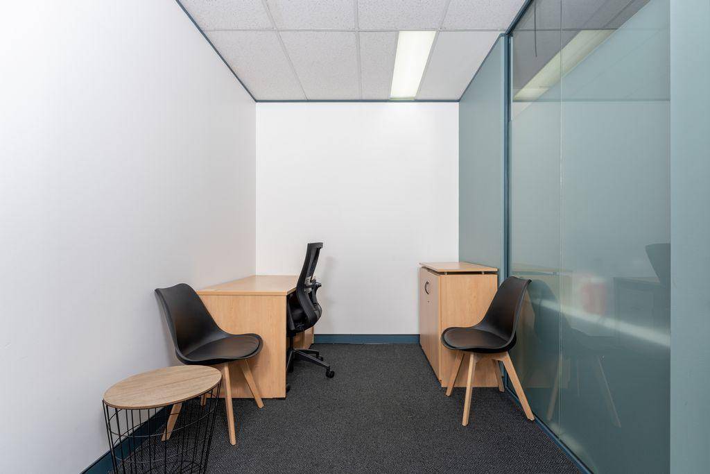 Kleines, helles Büro mit Holztisch, zwei Stühlen und einer modernen Glaswand für Privatsphäre.