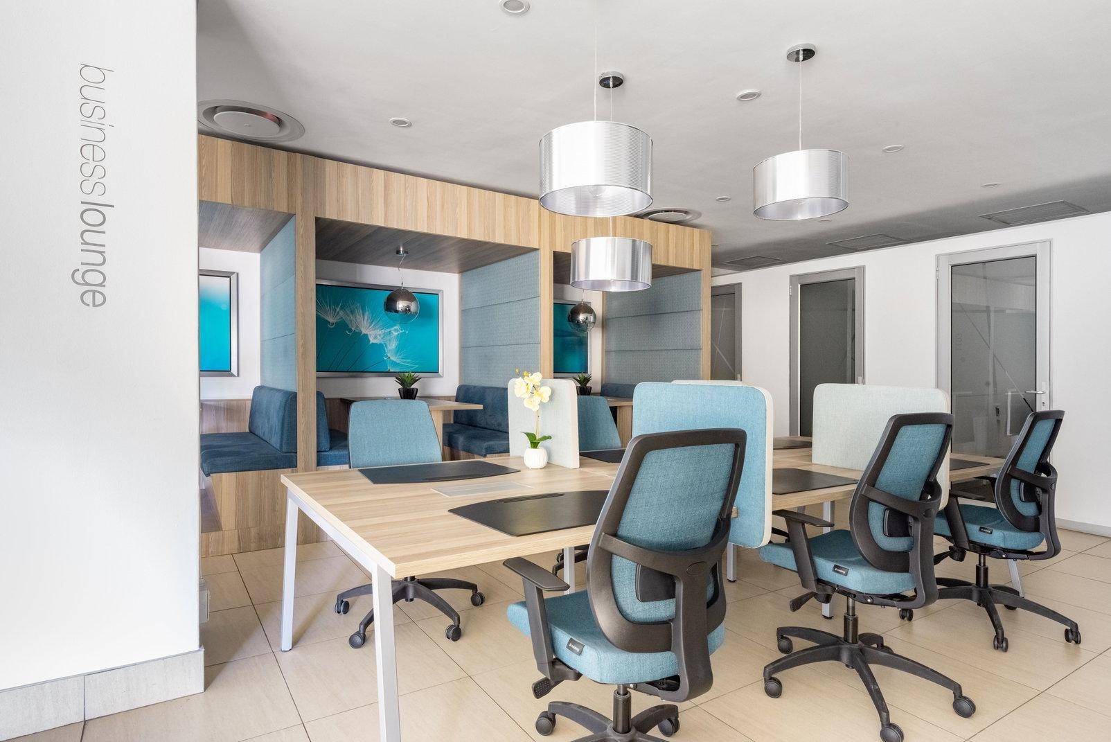 Moderne Business-Lounge mit verschiedenen Arbeitsbereichen, bequemen Sitzecken und stilvollen Hängelampen.