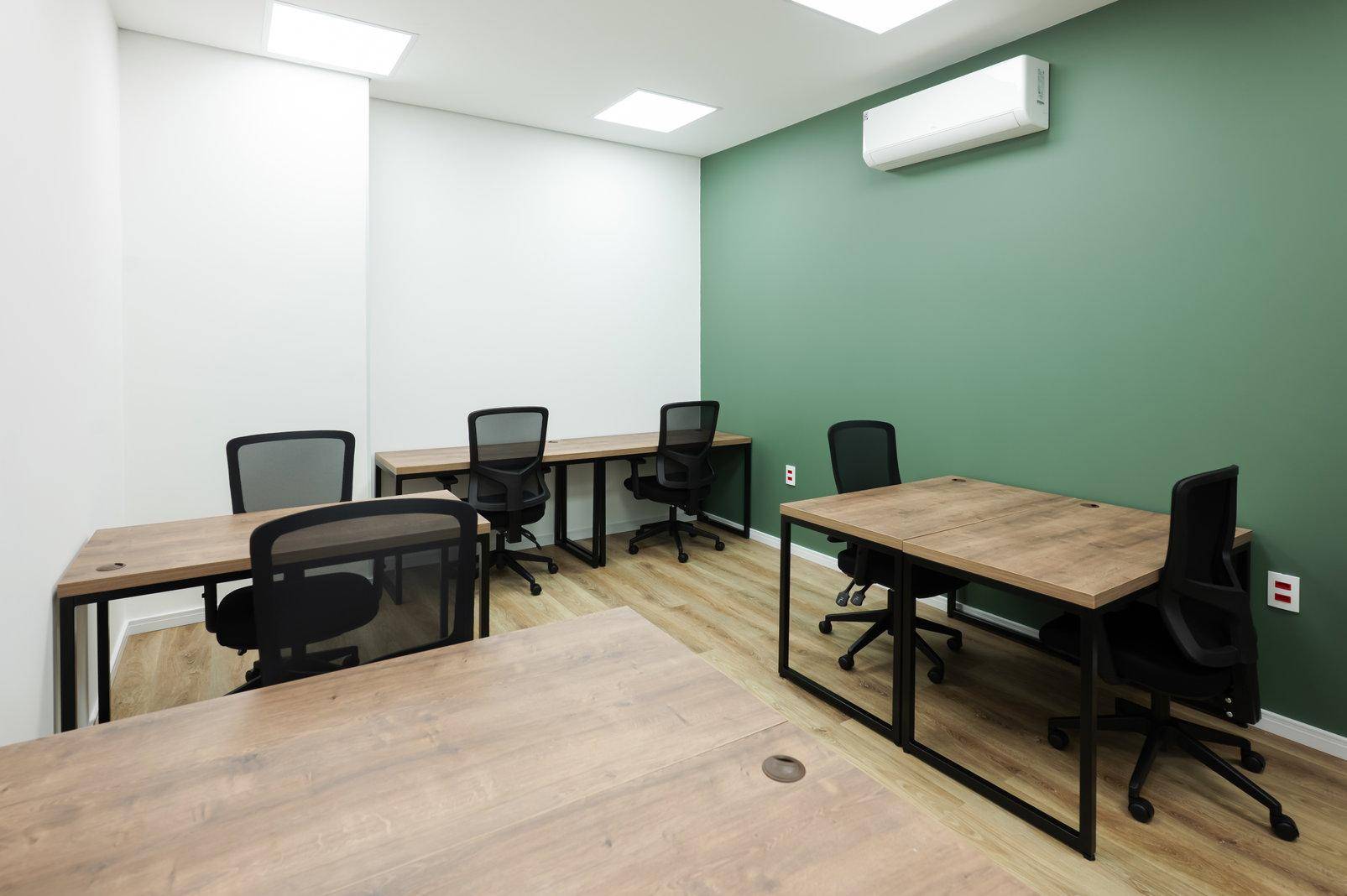 Modernes Büro mit grüner Akzentwand, Holztischen und Klimaanlage für angenehmes Raumklima.