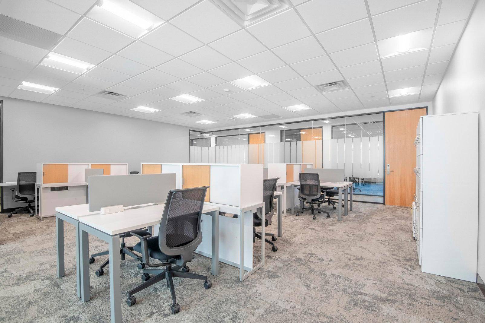 Modernes Großraumbüro mit modularen Arbeitsplätzen, Glasabtrennungen und Teppichboden.