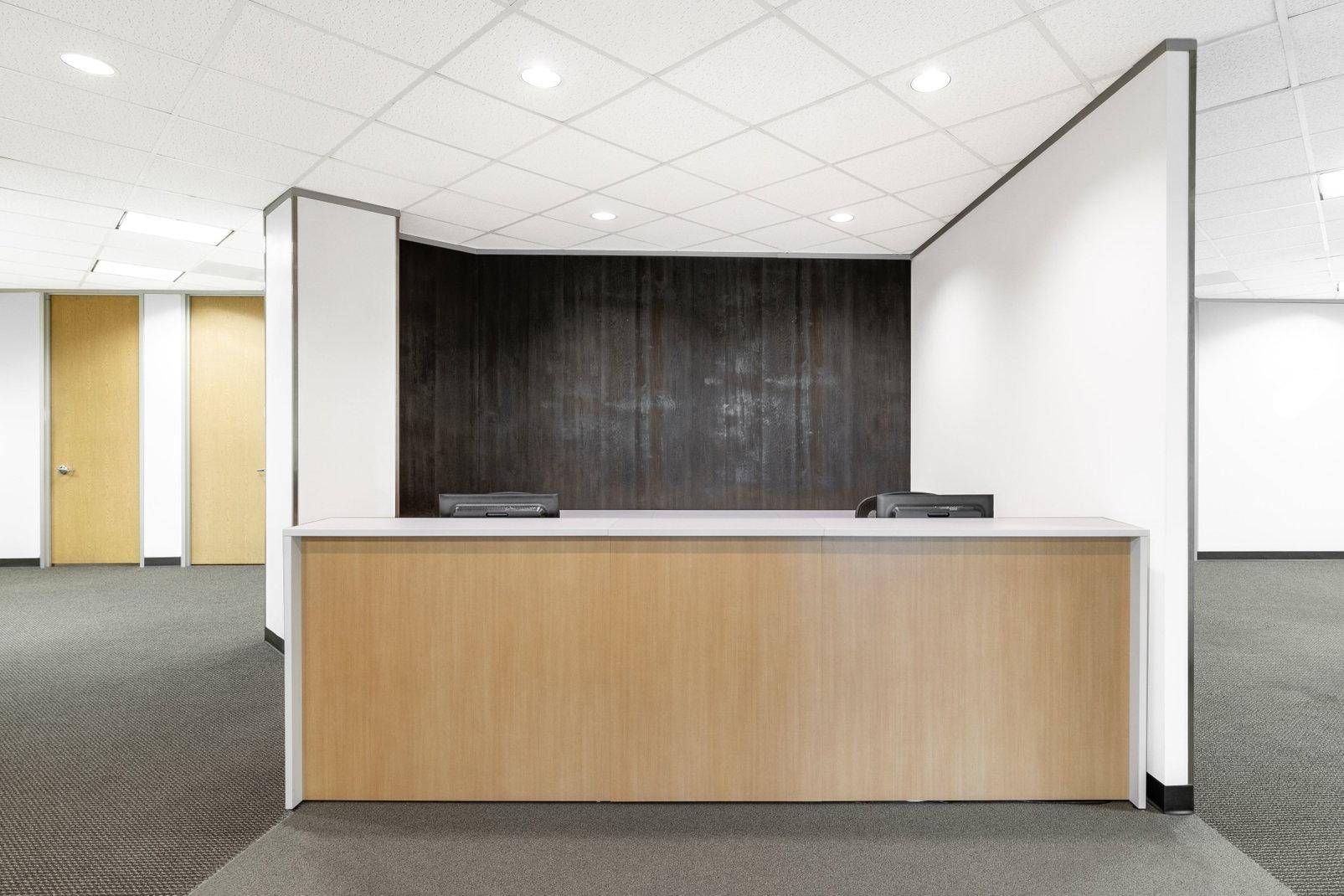 Empfangsbereich mit einer Holztheke, dunkler Akzentwand und Teppichboden in einem modernen Bürogebäude.