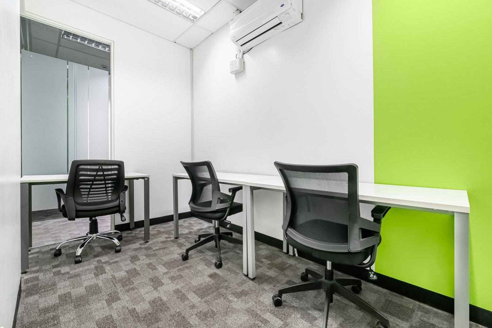 Kompaktes Büro mit drei Arbeitsplätzen, Teppichboden und einer hellgrünen Wand für frische Akzente.