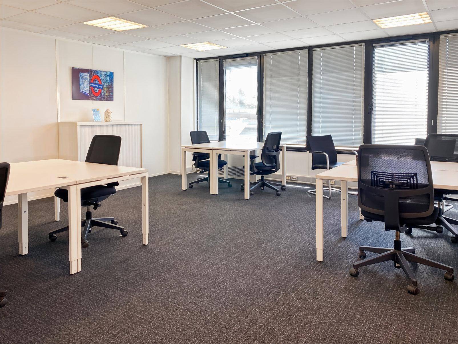 Modernes Büro mit mehreren Arbeitsplätzen, großen Fenstern und Jalousien für angenehmes Licht.